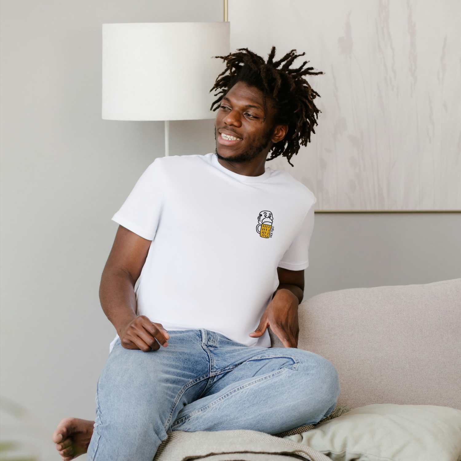 Lächelnder Mann mit Dreadlocks trägt das weiße Herren Bier T-Shirt Pack Maß auf dem Sofa sitzend.