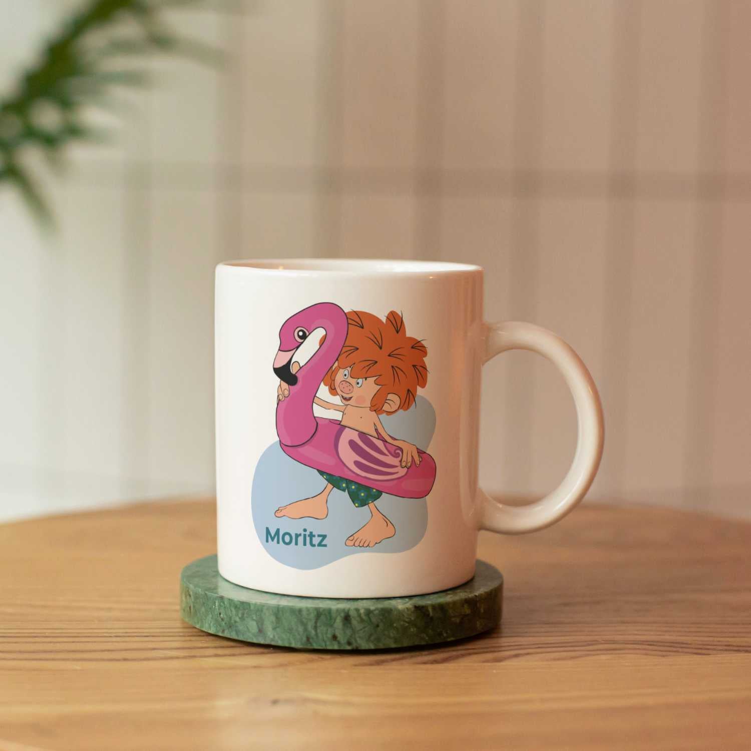 Personalisierte Pumuckl Tasse Badespaß mit Flamingo-Schwimmring und individualisiertem Namen Moritz auf grüner Unterlage.
