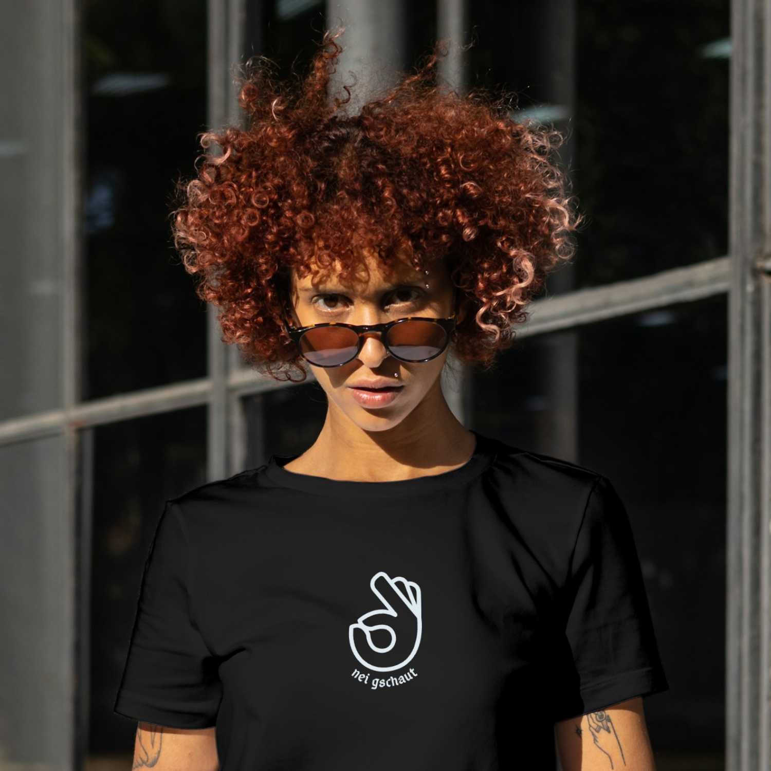 Damen T-Shirt Nei Gschaut in Schwarz, Model trägt blickdichte Sonnenbrille und hat rötliche Locken.