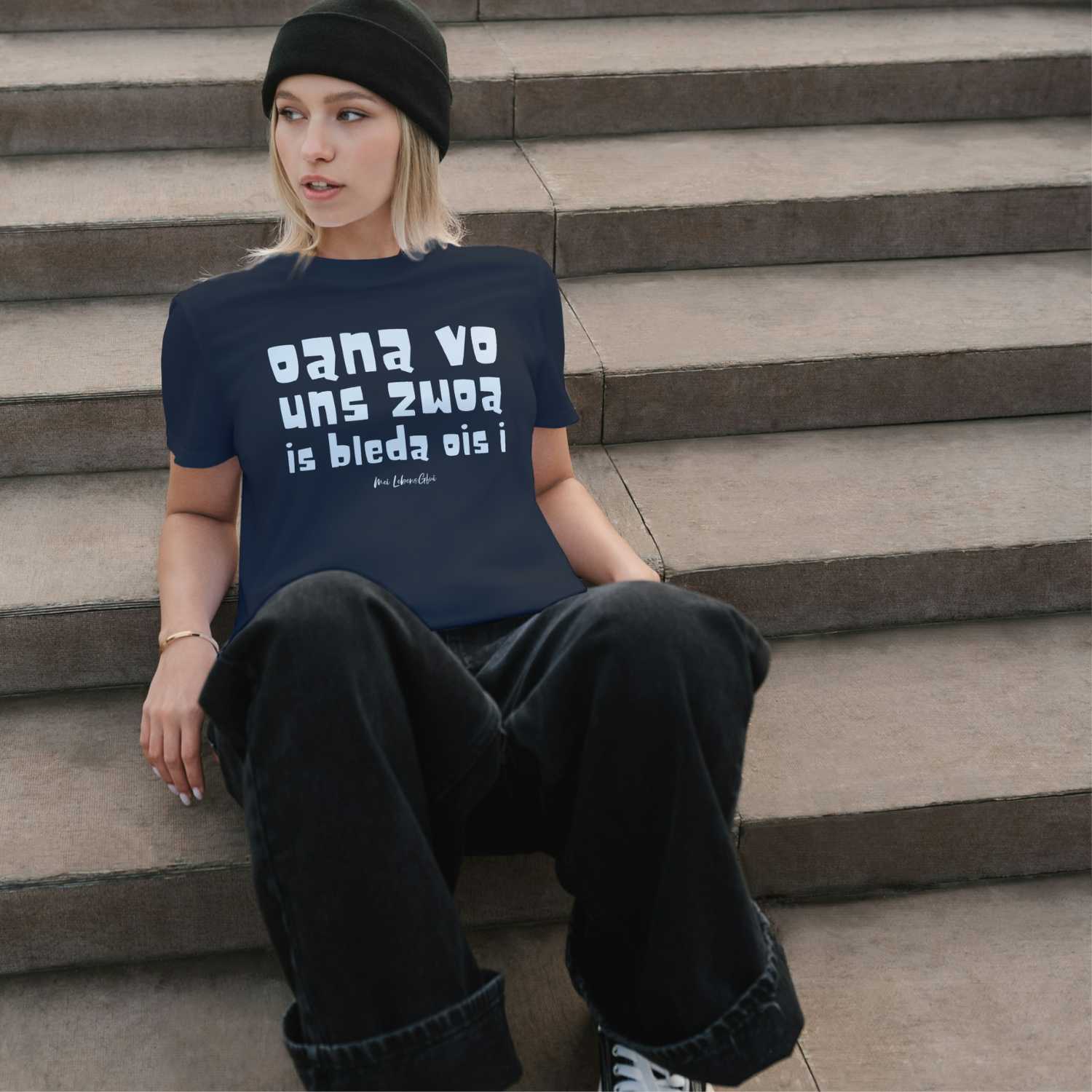 Junge Frau trägt dunkelblaues Damen T-Shirt "Oana vo uns zwoa" mit weißem Spruch und schwarze Hose sitzend auf Treppe.