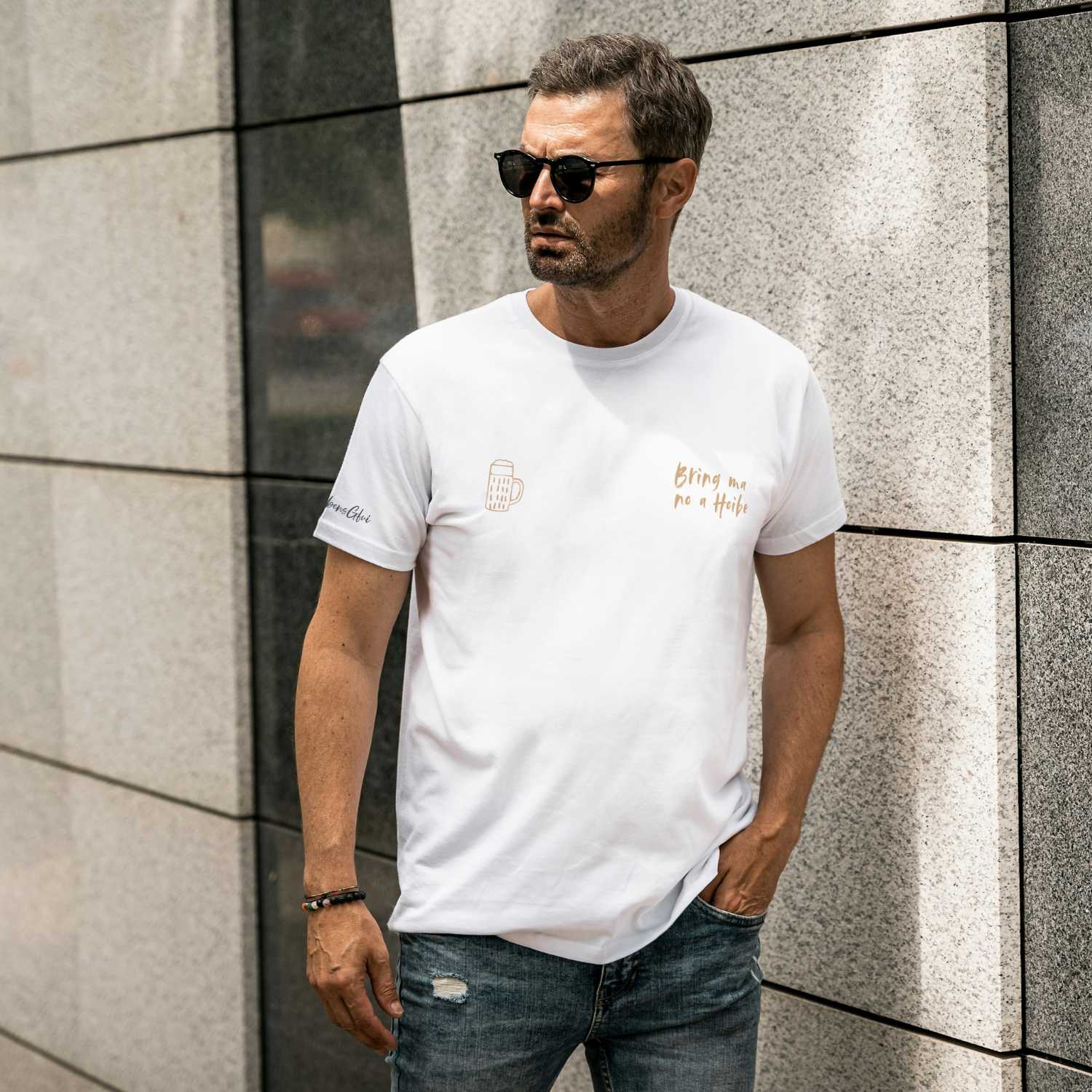 Herren T-Shirt Bring ma no a Hoibe in Weiß, goldener Druck und Bierkruglogo, urbaner Hintergrund.