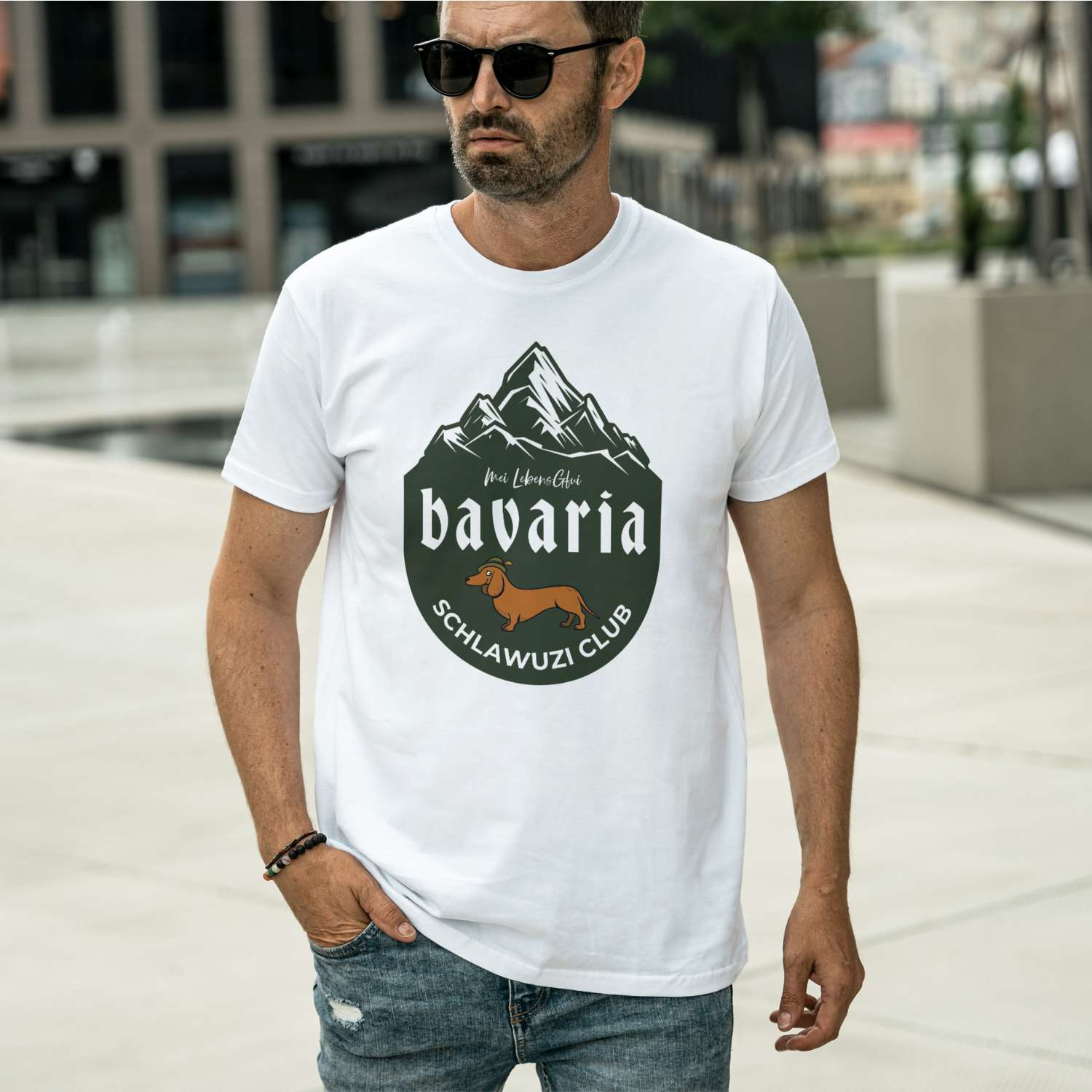 Mann trägt weißes Herren T-Shirt "Bavaria Schlawuzi Club" mit dunklem Berg-Motiv und Dackel-Druck.