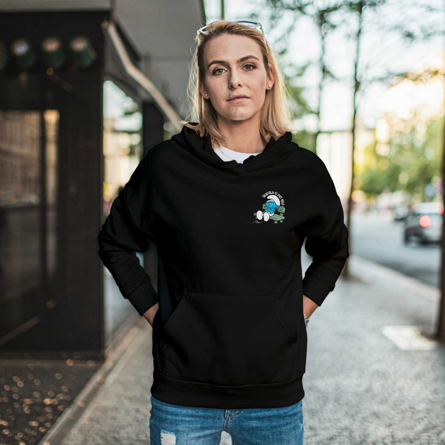 Junge Frau trägt schwarzen Damen Hoodie "Grantln is mei Yoga" mit Schlumpf auf Parkbank im Stadtbild.