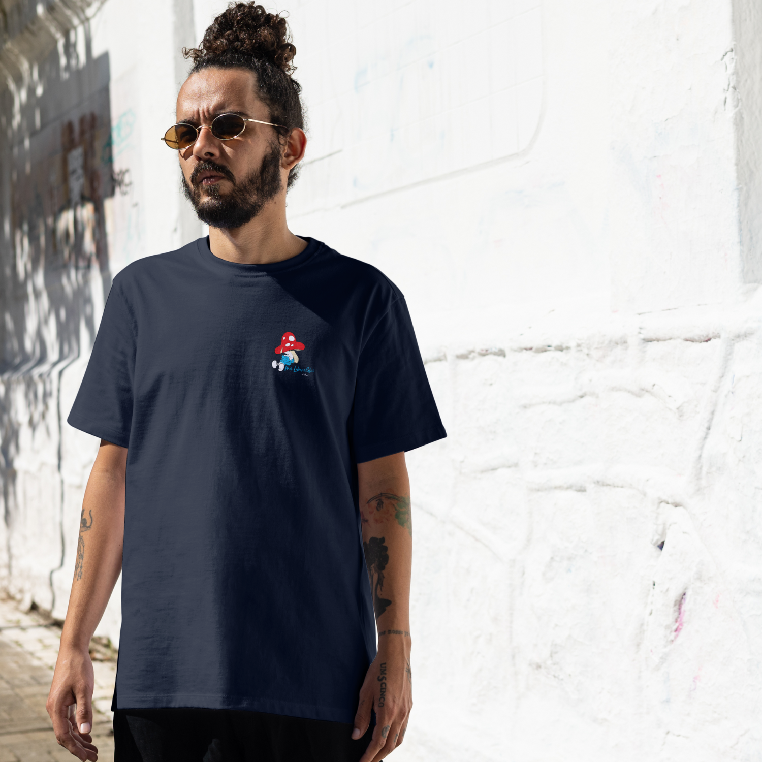 Junger Mann in ®Die Schlümpfe Herren T-Shirt Do legst di nieda mit Pilz-Motiv vor weißer Wand