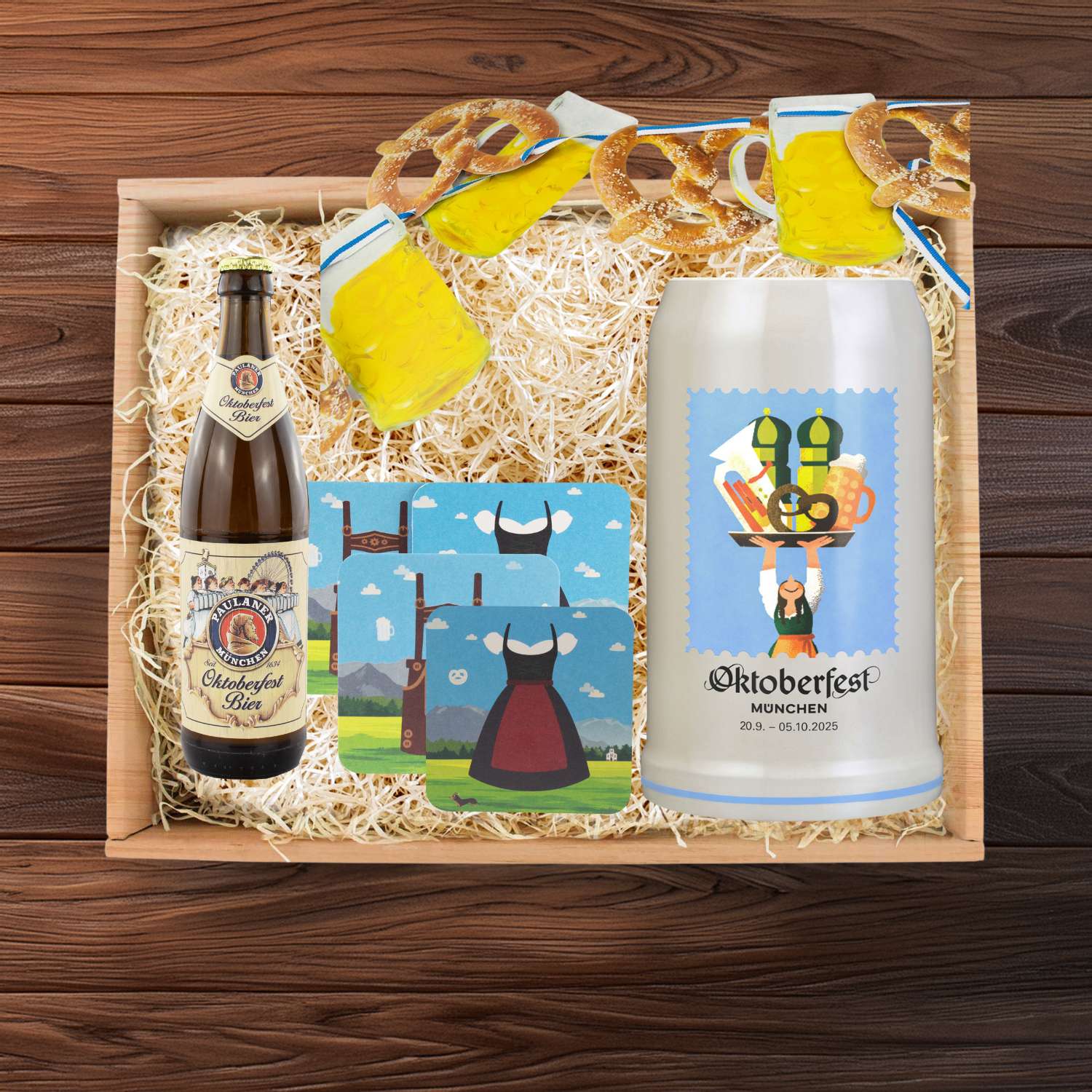 Oktoberfest-Box Wiesnkrug & Deko mit Paulaner Bierflasche, bedrucktem Krug, Untersetzern und Brezelgirlande auf Stroh.