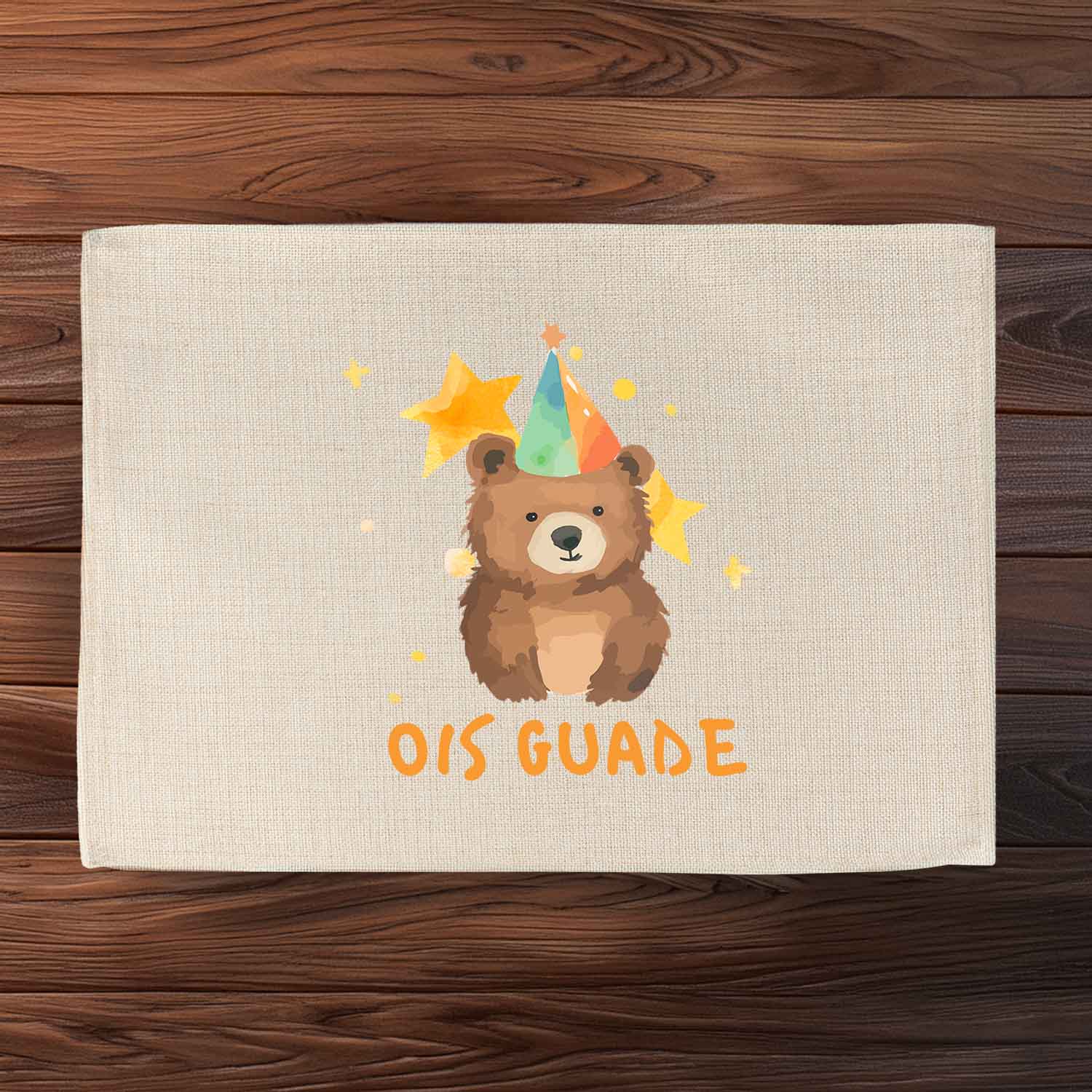 Beiges Tischset "Ois Guade Bär" mit niedlichem Bären, Partyhut, Sternen und Schriftzug auf Holzuntergrund.