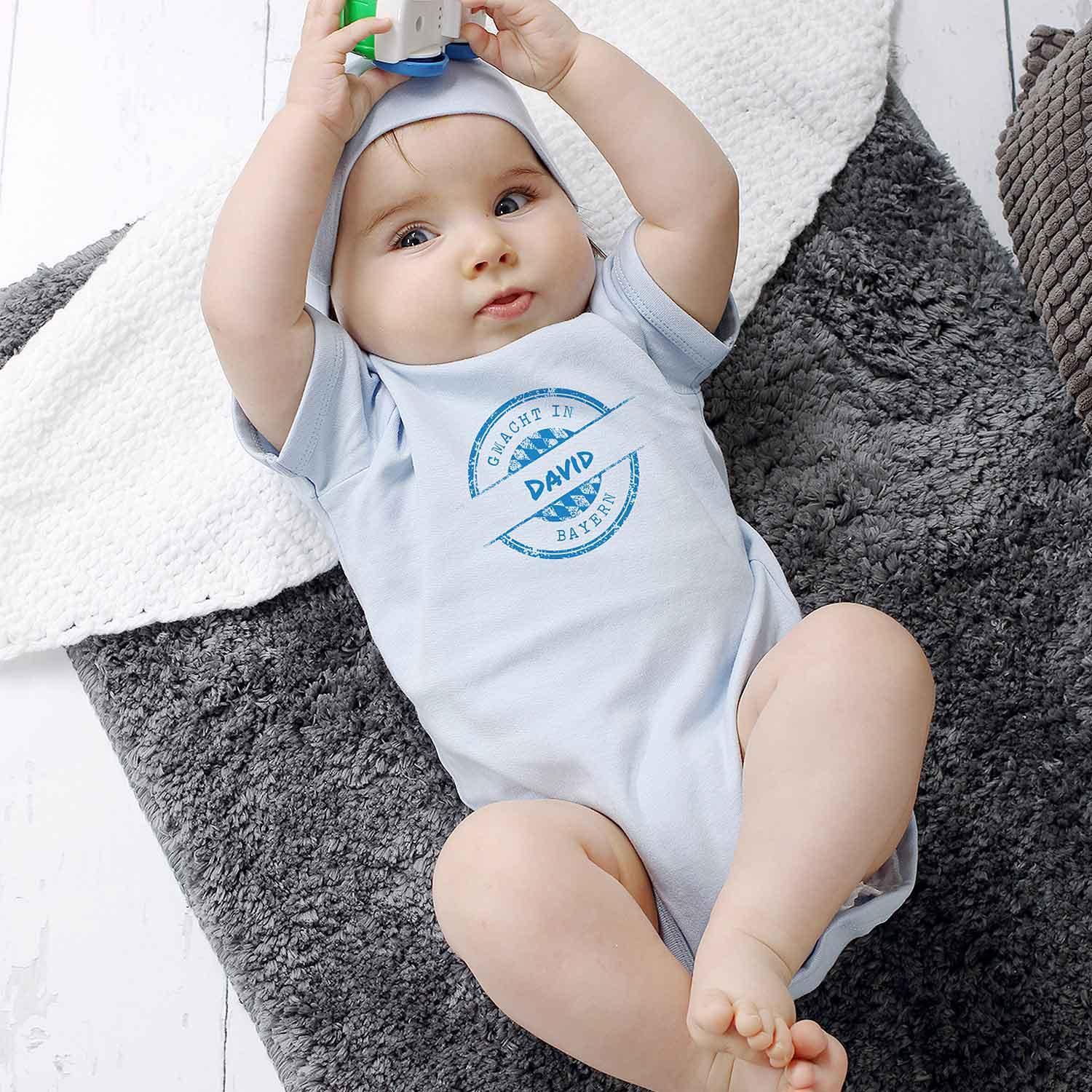 Baby Body gmacht in Bayern in Hellblau mit Schriftzug David, liegt auf flauschiger Decke