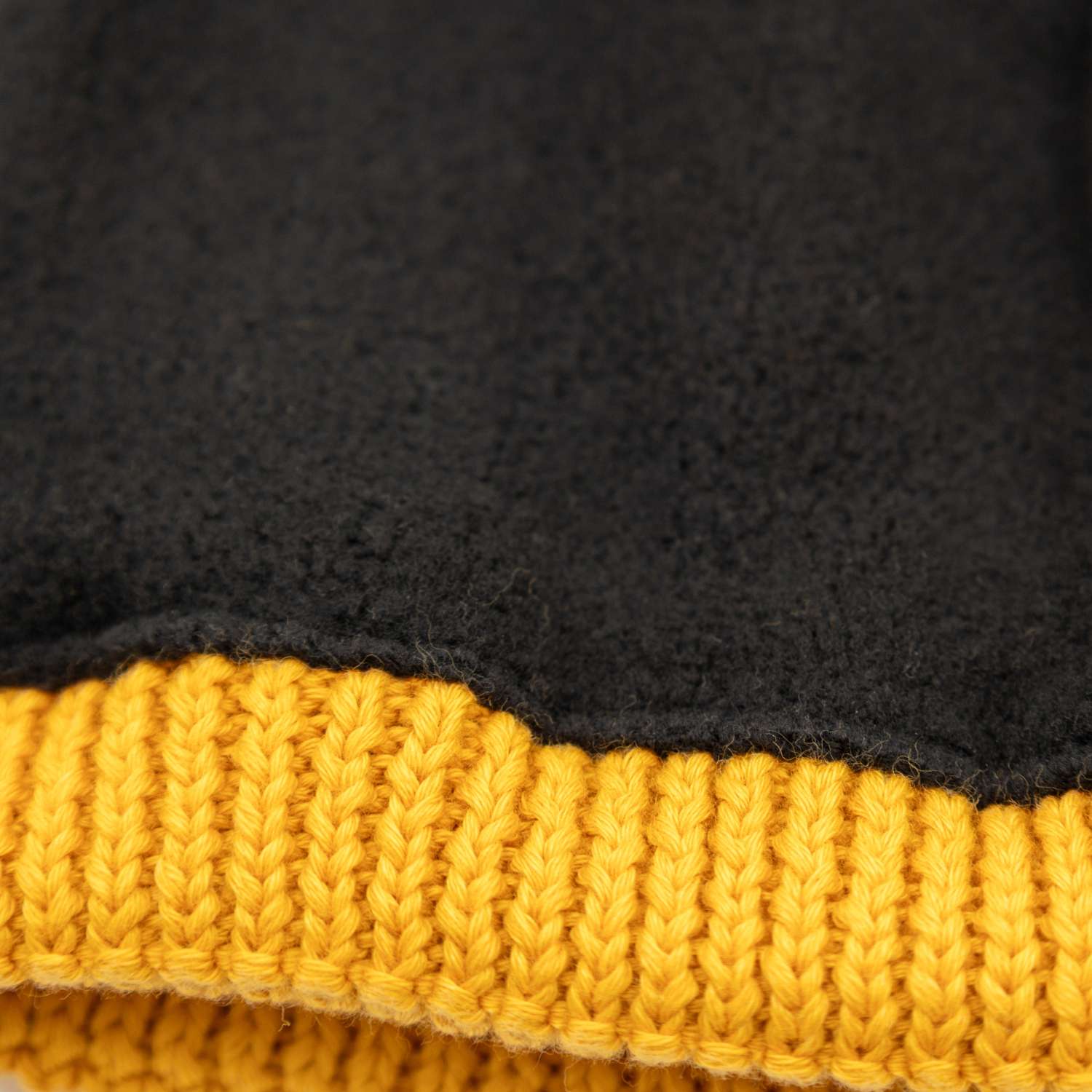 Detaillierte Nahaufnahme der ®Pumuckl Beanie aus Baumwolle mit schwarzem Stoff und gelbem Rippstrickbund.