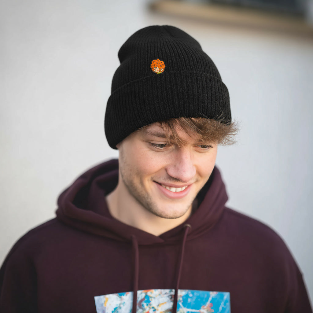 Mann trägt ®Pumuckl Beanie aus Baumwolle in Schwarz mit orangefarbenem Meister Eder Logo, lächelnd