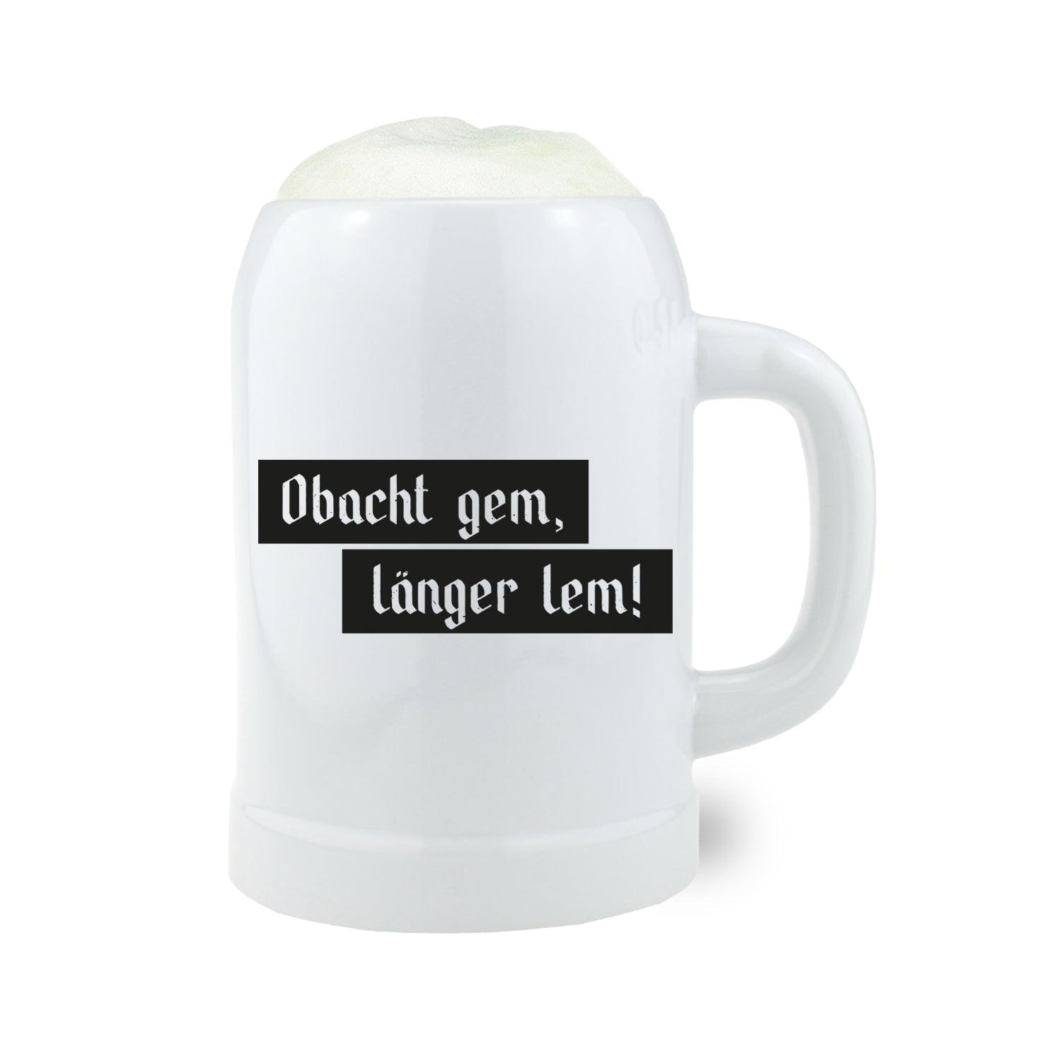 Weißer Keramik Bierkrug Obacht gem, mit schwarzem Schriftzug "Obacht gem, länger lem!" und Bierschaum