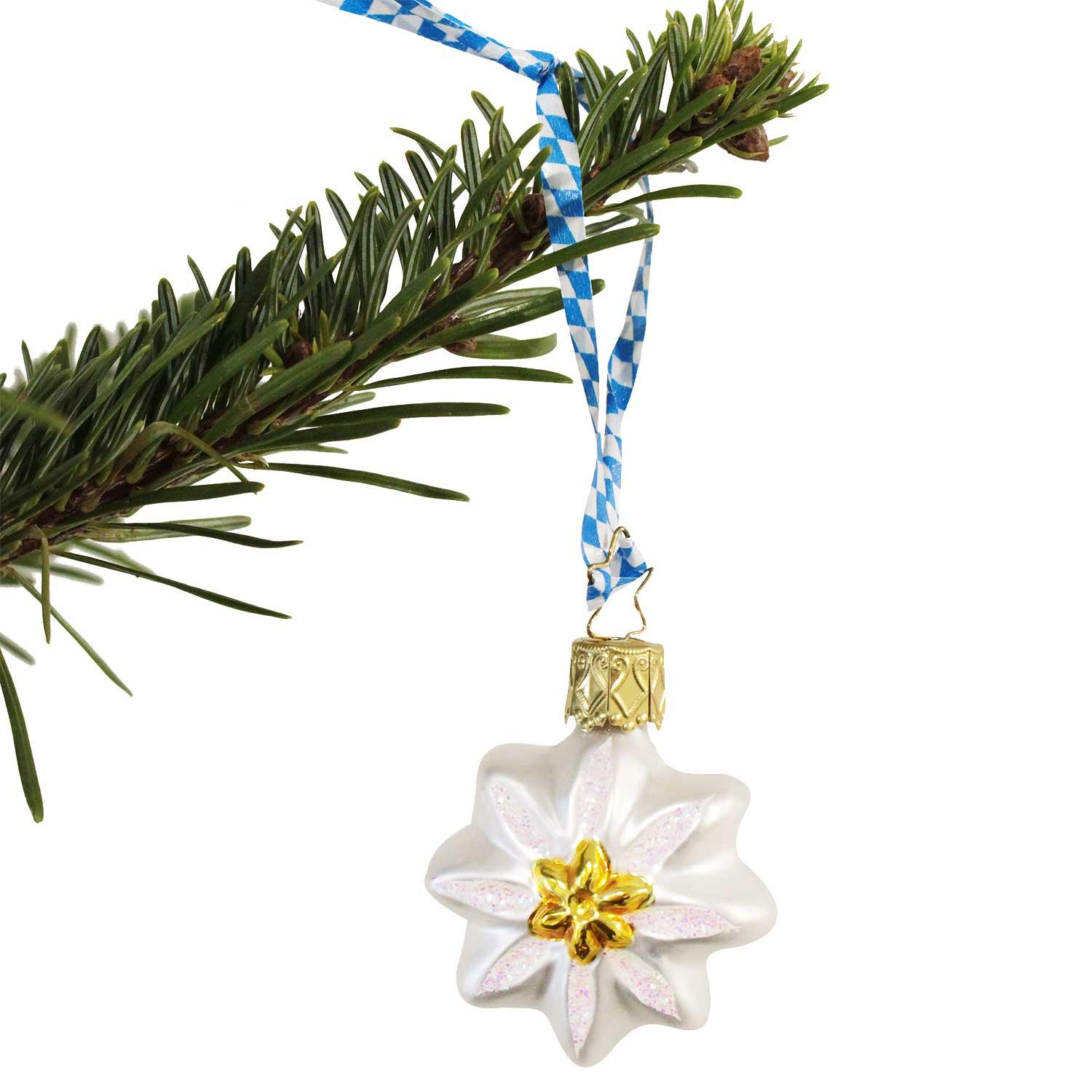 Gläserner Christbaumschmuck in Edelweißform mit goldener Mitte und bayerischem blau-weißem Band am Tannenzweig.
