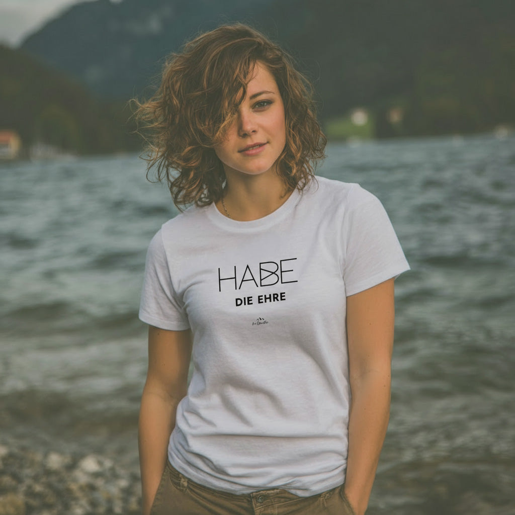 Junge Frau in weißem Damen T-Shirt "Habe die Ehre" mit Schriftzug am Seeufer.