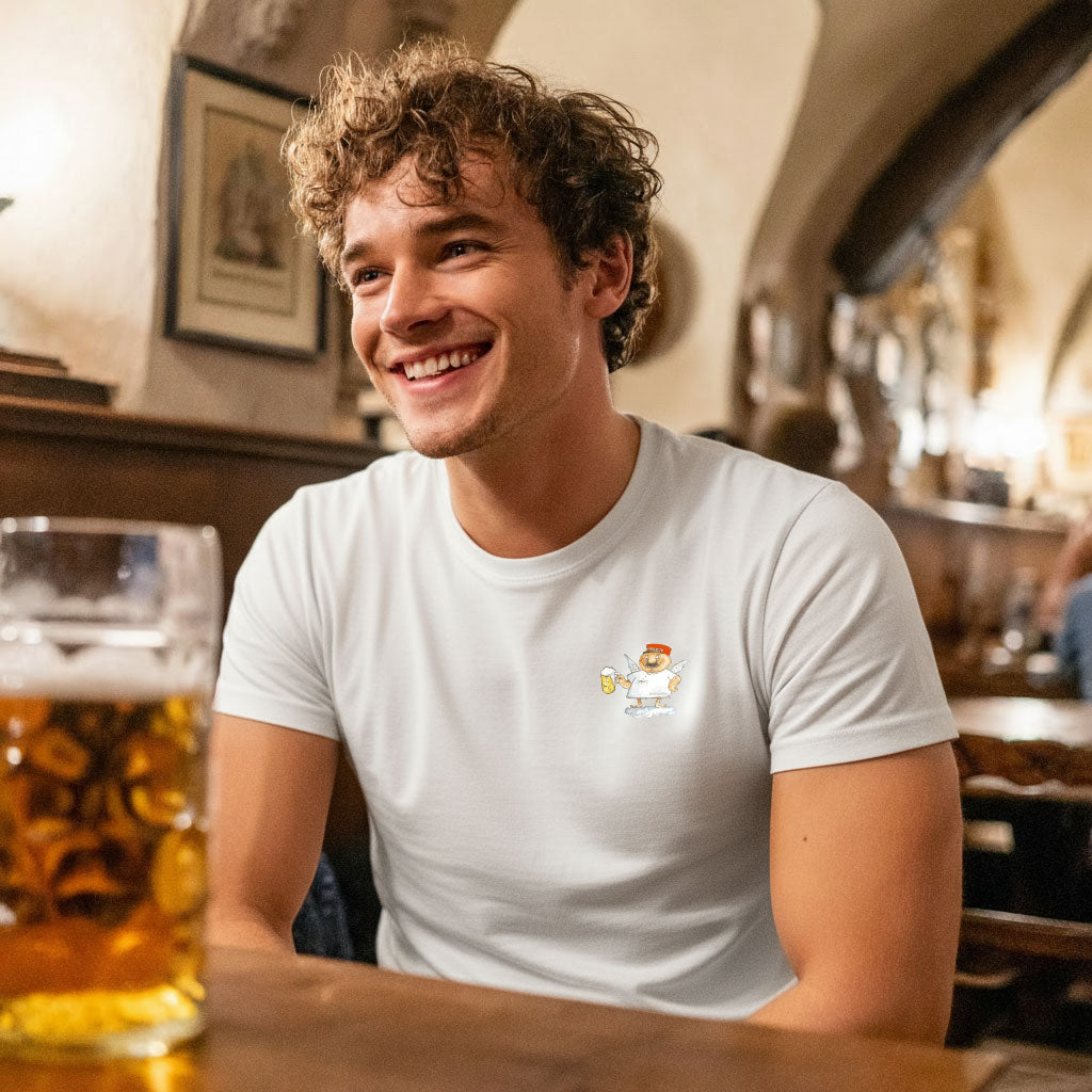 Lachender Mann im weißen Engel Aloisius Herren T-Shirt "A Bier sag i", sitzt mit Bierkrug an Holztisch.