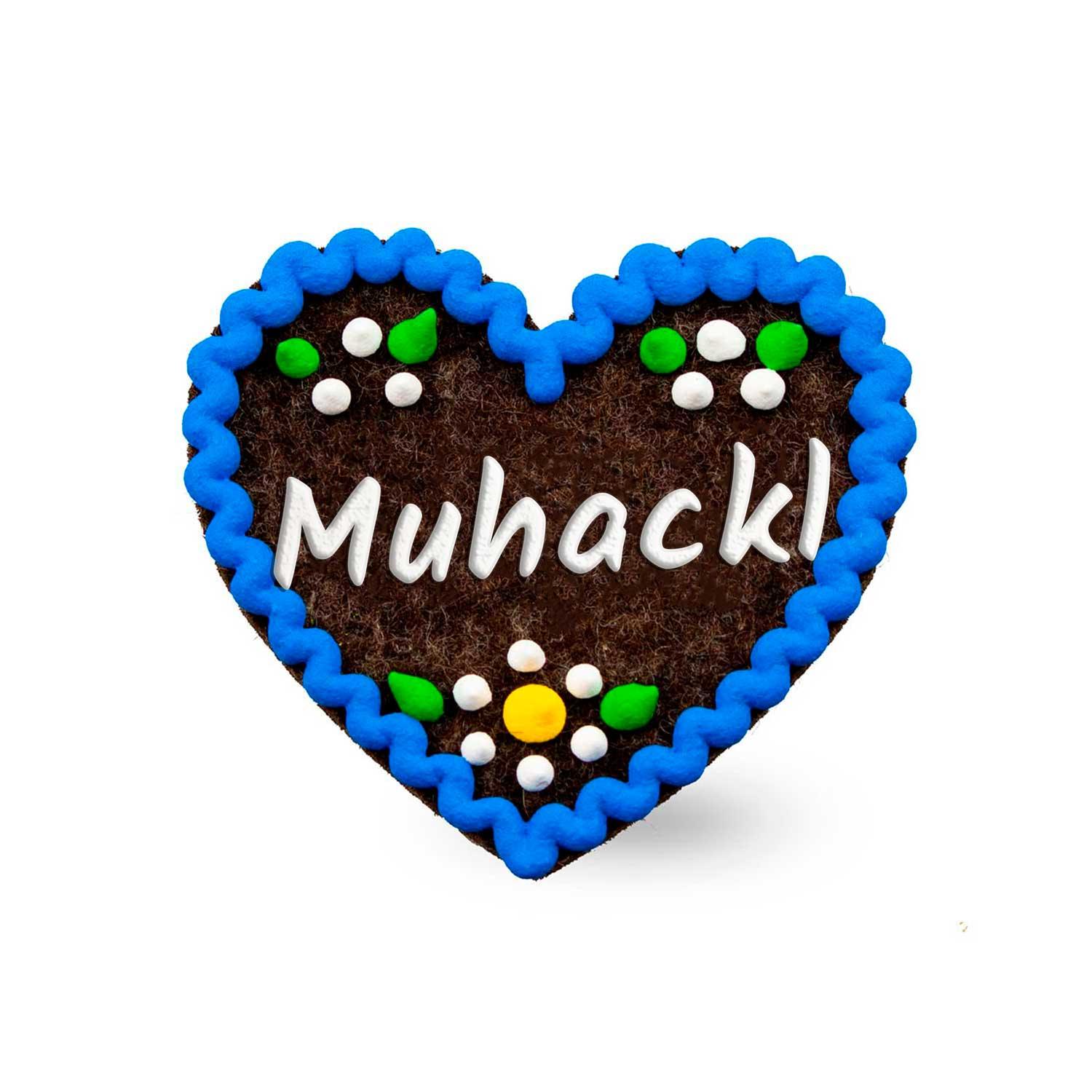 Brauner Filzherz-Anstecker "Muhackl" mit blauem Rand, weißen Blüten und bunten Verzierungen, weißer Schrift.