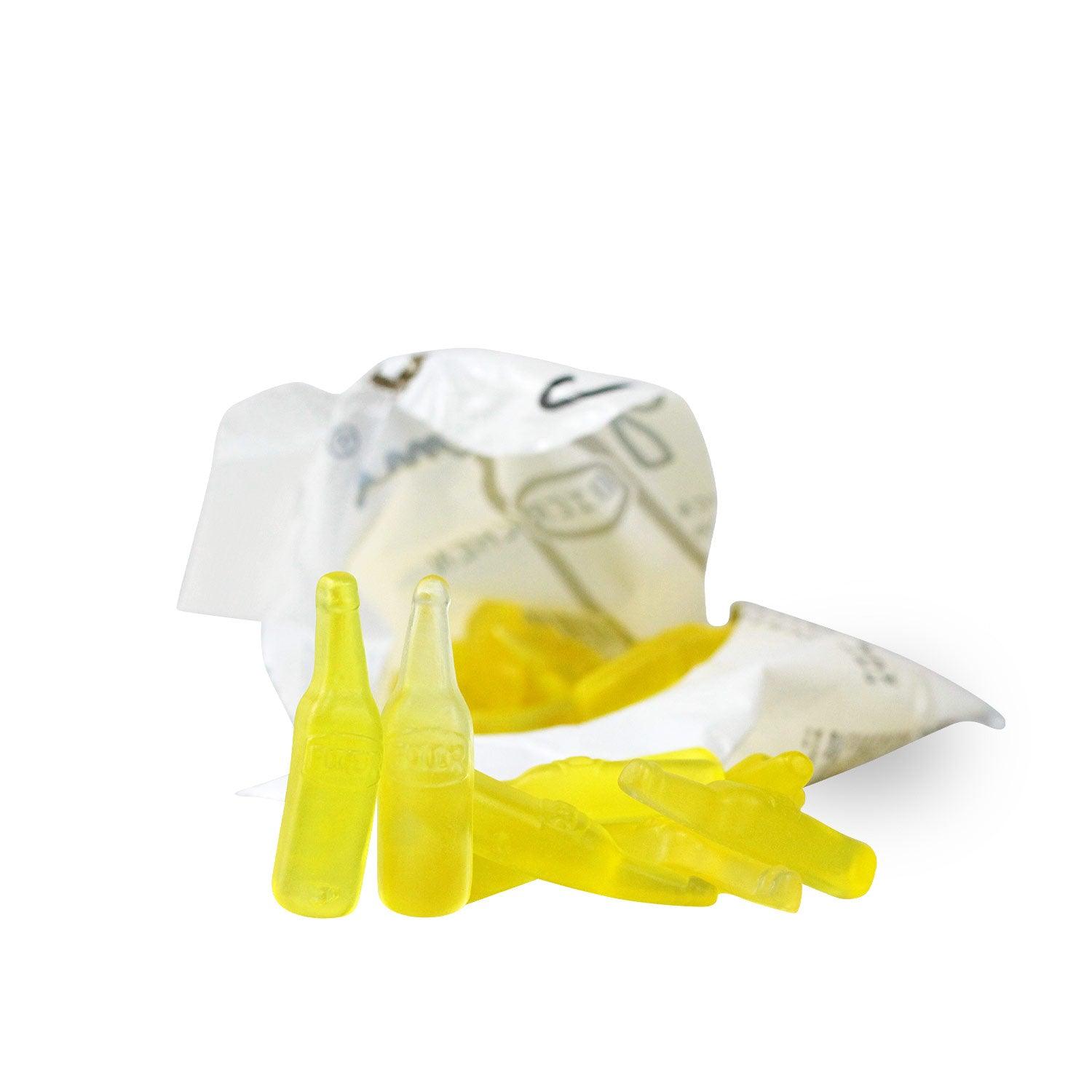 Gelbe Gummibierchen Fruchtgummis in Flaschenform, teils aus geöffneter Verpackung quellend, auf weißem Grund.
