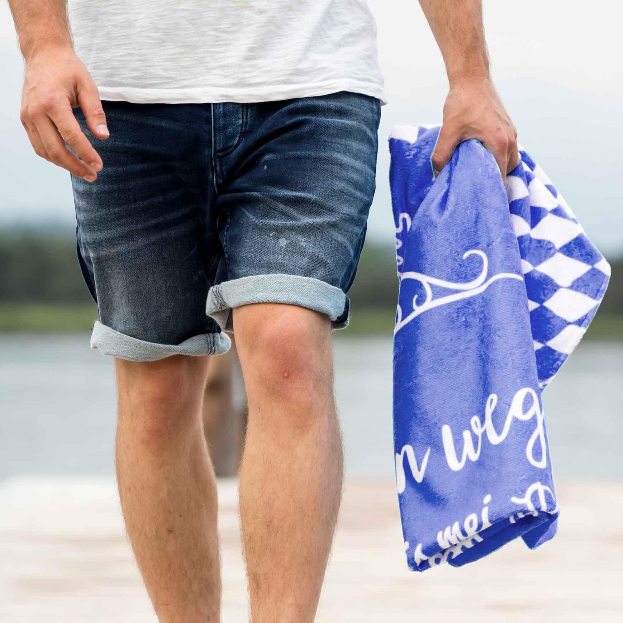 Sonnige Aussicht auf ein blaues Handtuch mit weißer Schrift und Rautenmuster, lässig über den Arm getragen.