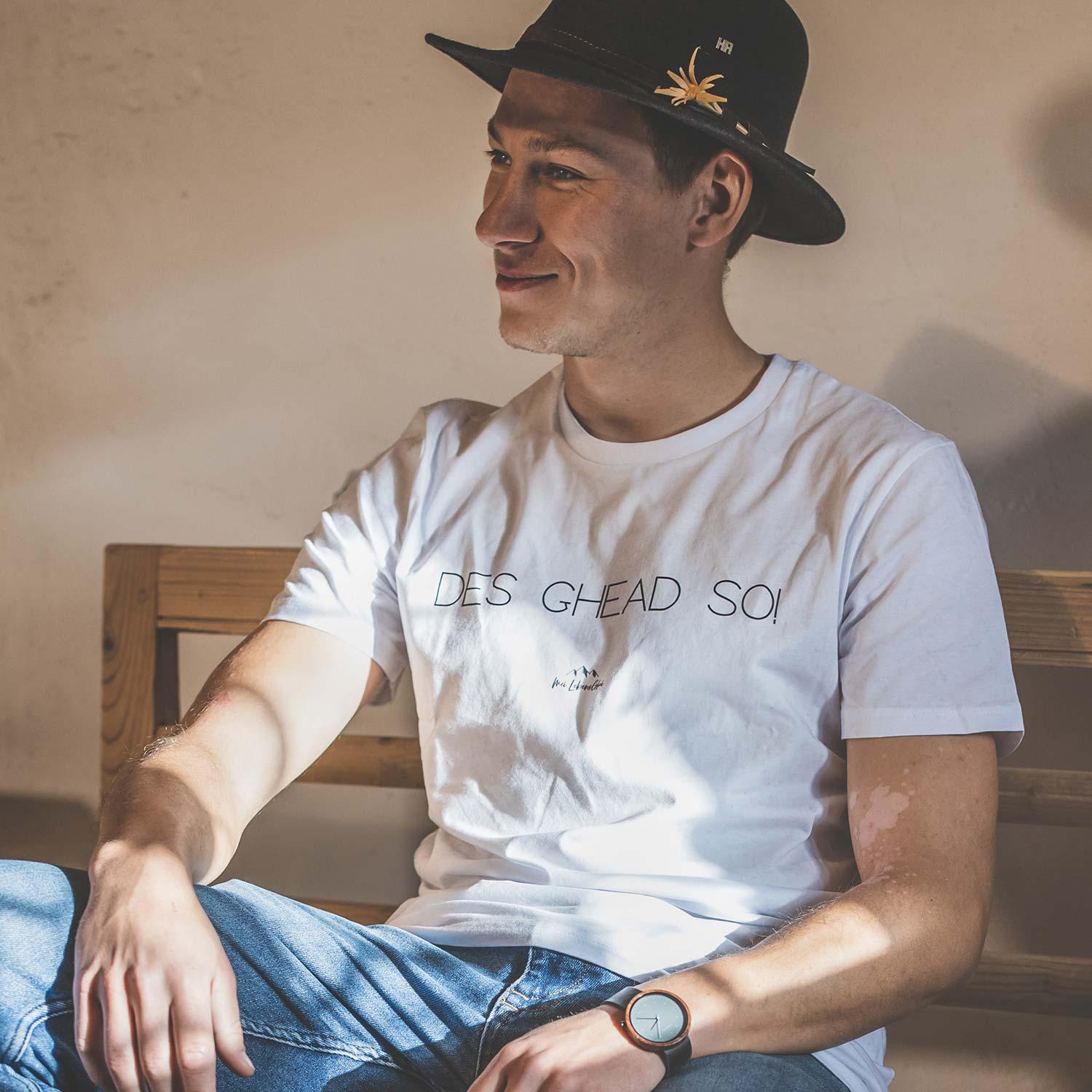 Lachender Mann im schwarzen Hut und weißem Herren T-Shirt Des ghead so!, entspannt sitzend
