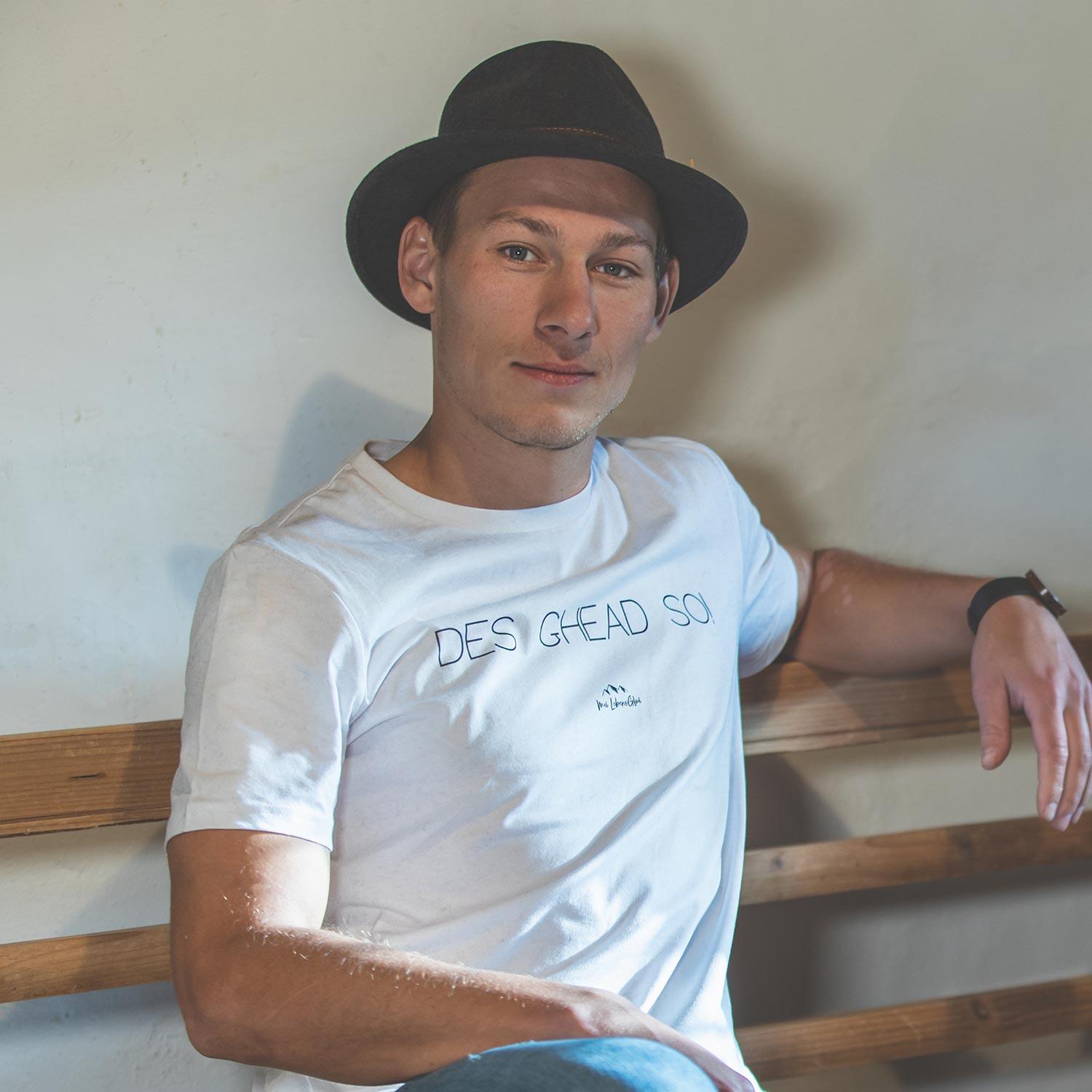 Junger Mann mit schwarzem Hut trägt weißes Herren T-Shirt Des ghead so! lässig auf einer Holzbank.