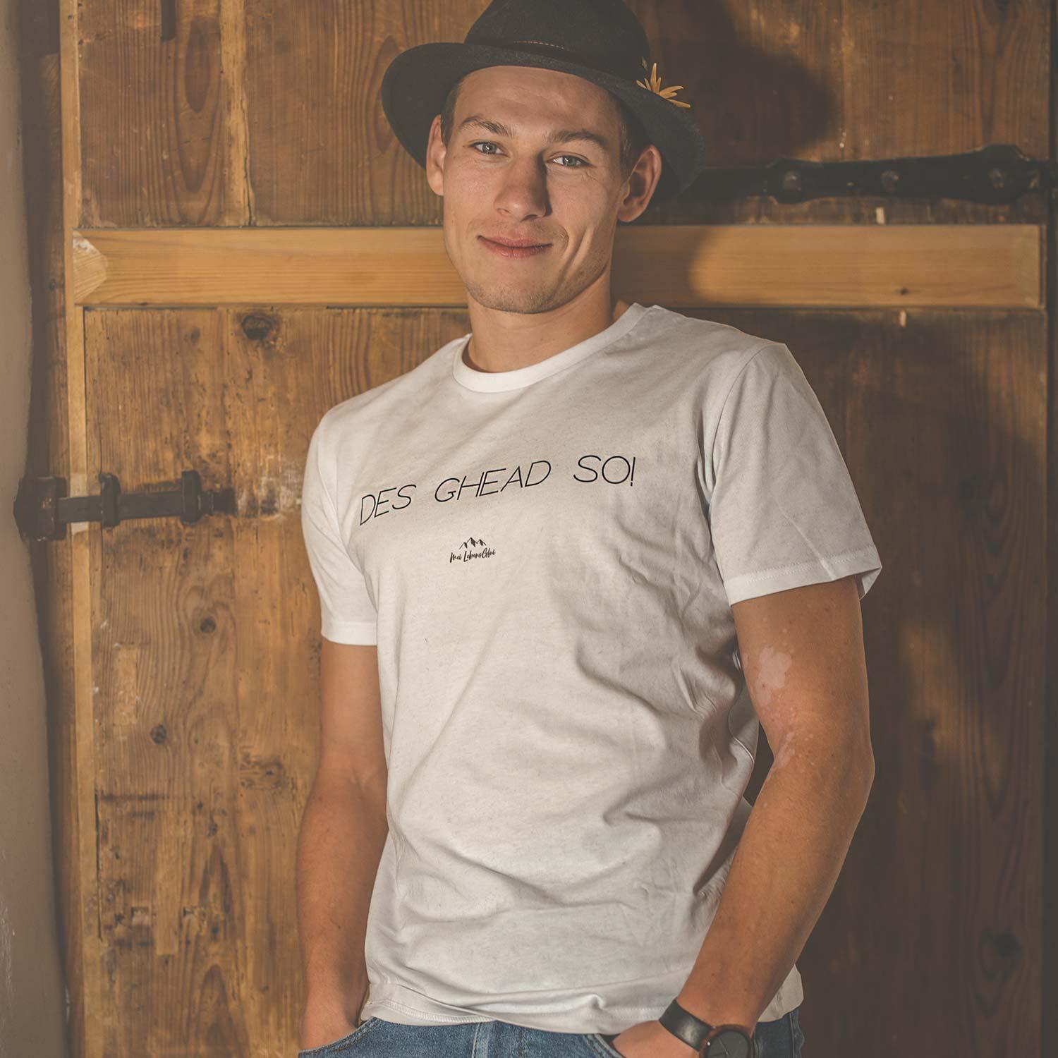 Junger Mann im schwarzen Hut und weißen Herren T-Shirt Des ghead so! vor rustikaler Holztür lachend.