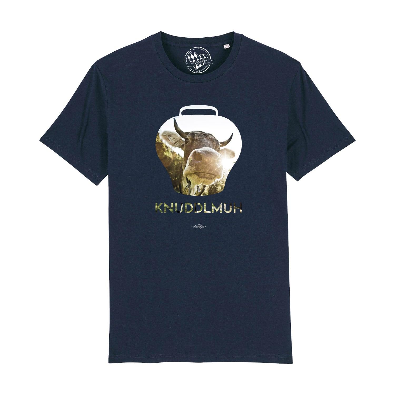 Dunkelblaues Herren T-Shirt Knuddlmuh mit stilisiertem Kuhglockenmotiv und Kuhgesicht in sonniger Berglandschaft.