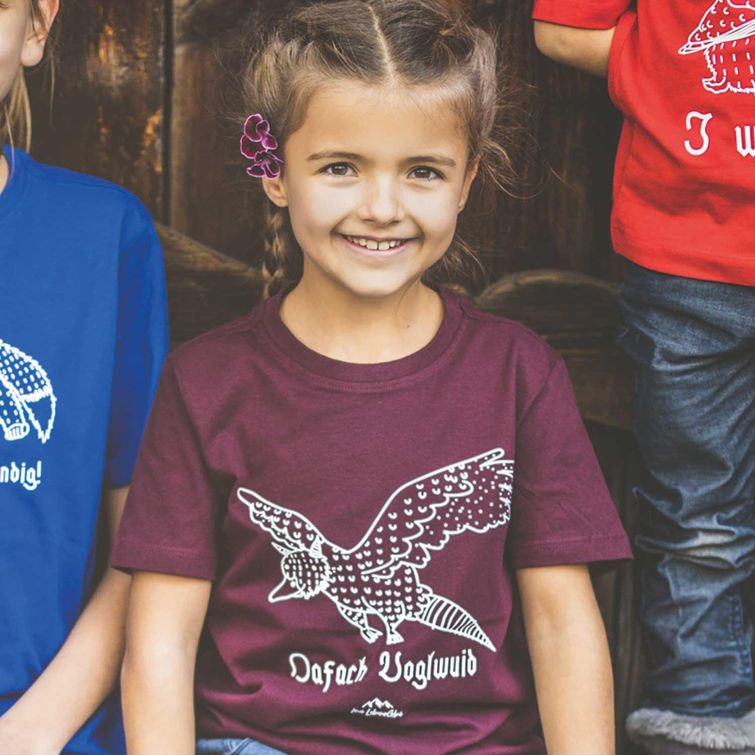 Lachendes Mädchen im bordeauxroten Kinder T-Shirt Wolpertinger Oafach Voglwuid mit weißem Motiv
