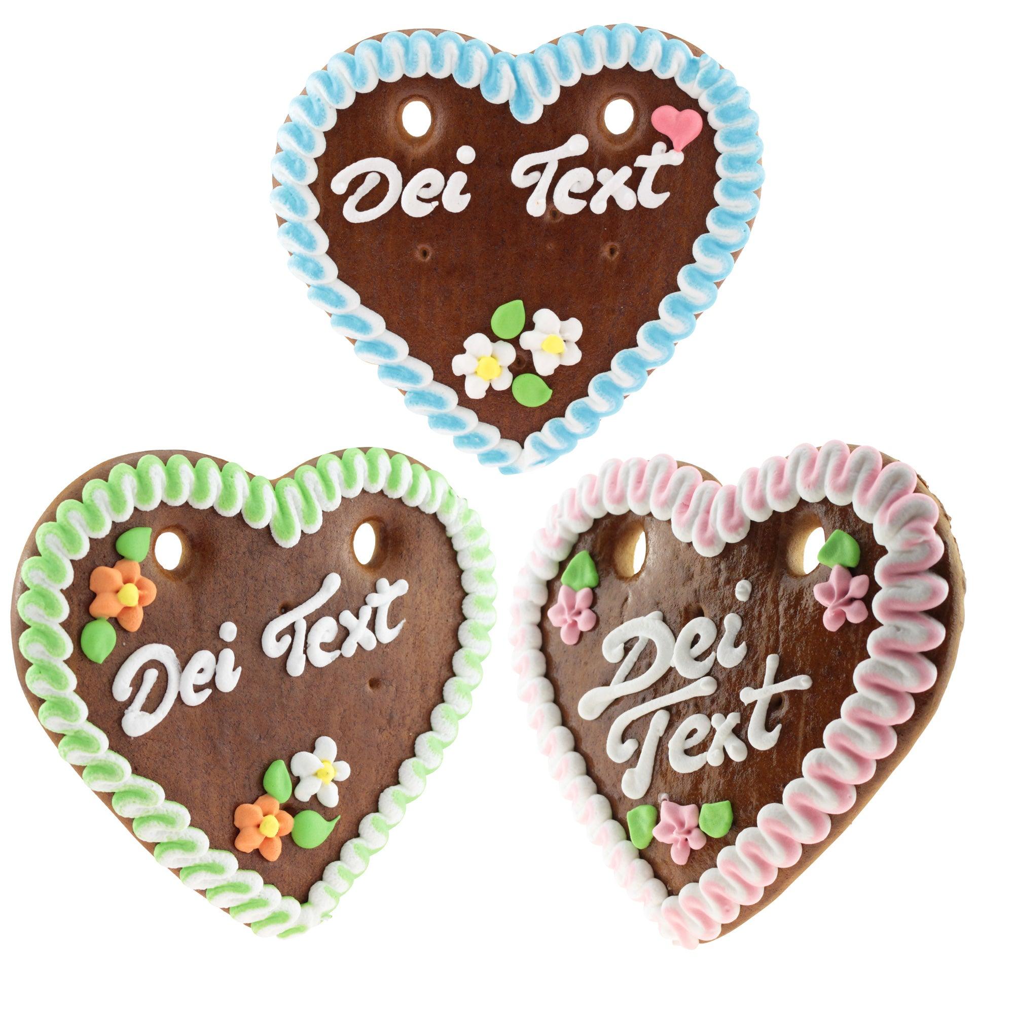 Drei Lebkuchenherzen mit personalisierbarem Text "Dei Text", verziert mit bunter Zuckerschrift und Blumen.