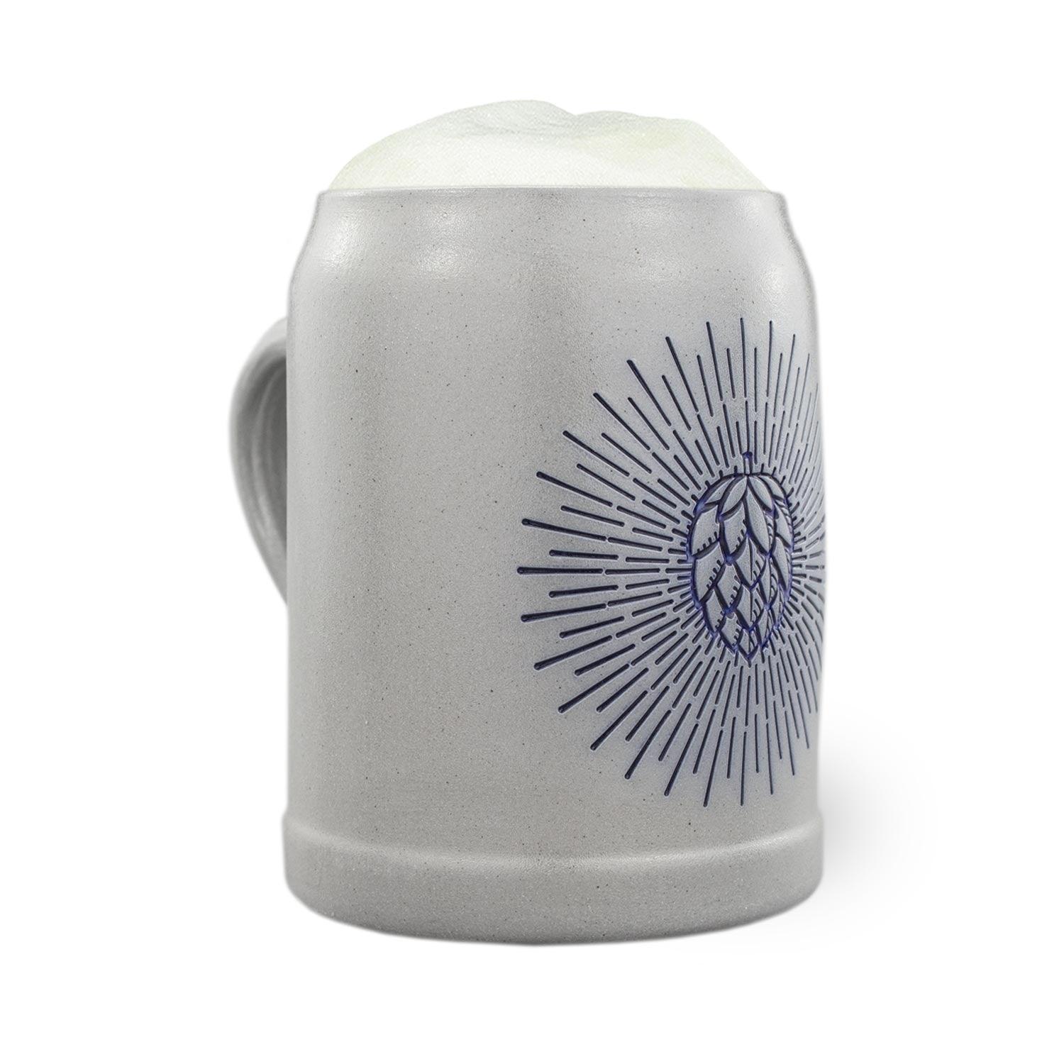 Grauer PREMIUM Bierkrug Holy Hopfen mit blauer Hopfendolde und Strahlenmuster, gefüllt mit Schaum.