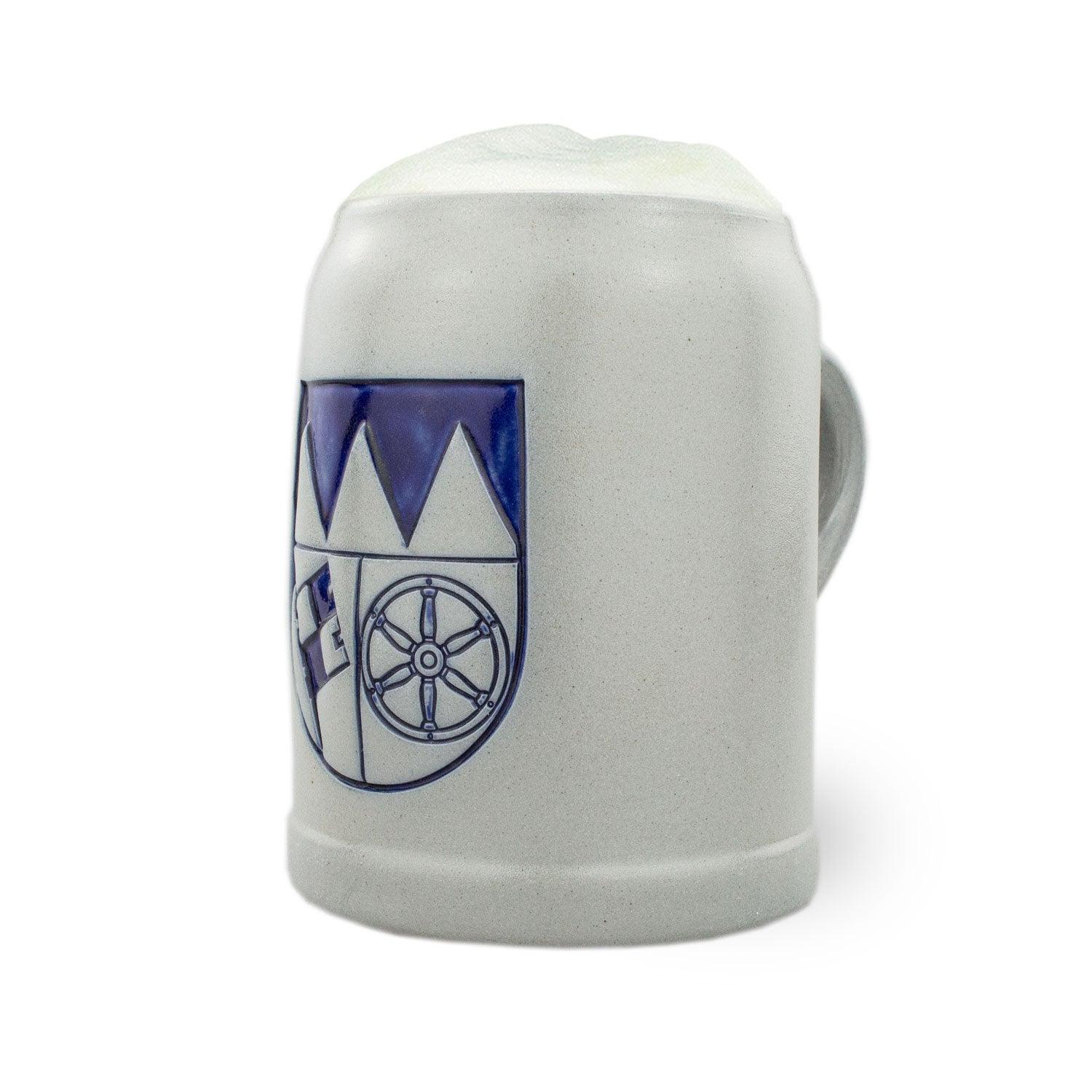 PREMIUM Bierkrug Unterfranken, steinzeugfarbener Krug mit blauem Wappen und frischem Bierschaum am Rand.