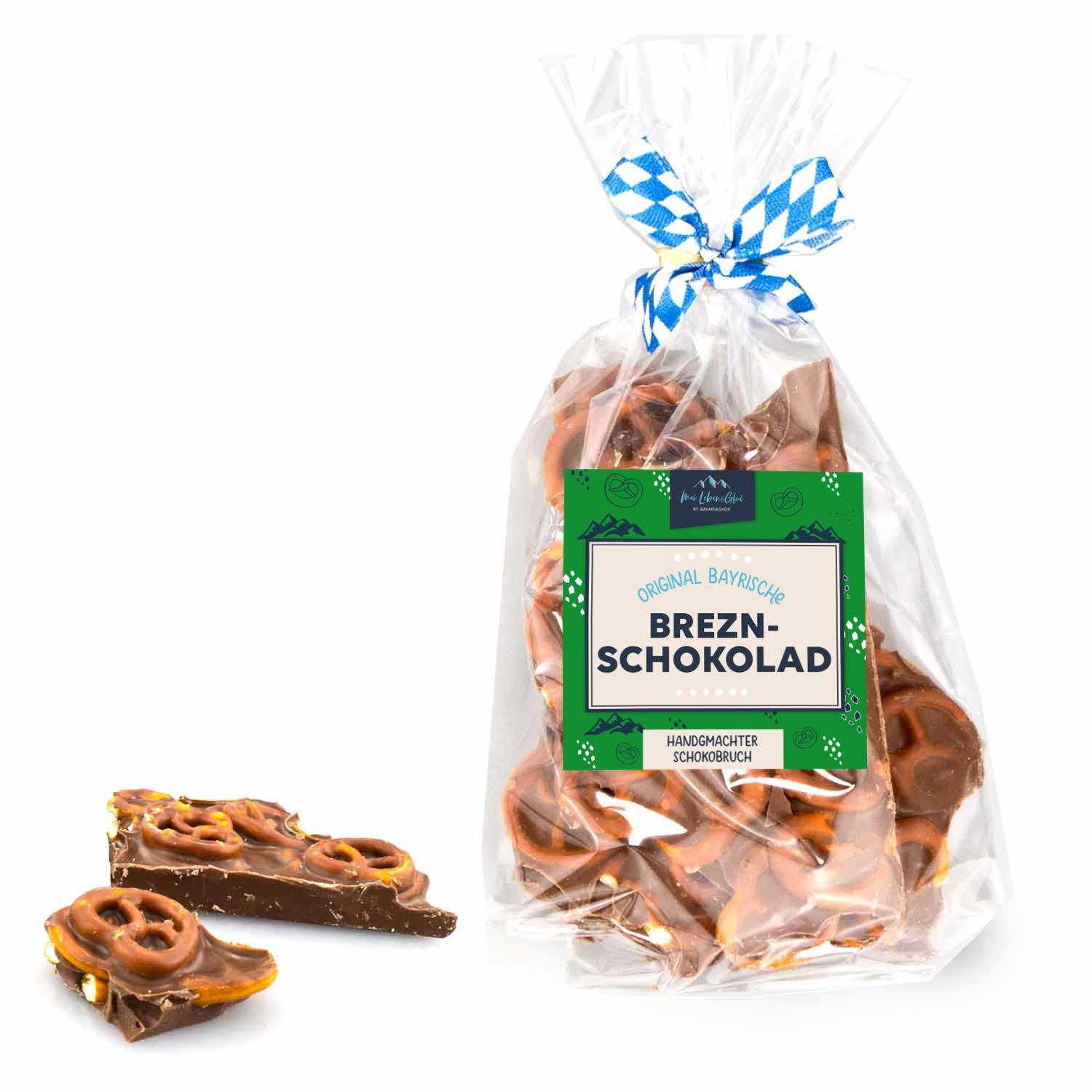 Schoko-Bruch mit Knusper-Brezn in transparenter Geschenktüte, blau-weiß karierter Schleife und Label. Einzelne Stücke liegen daneben.