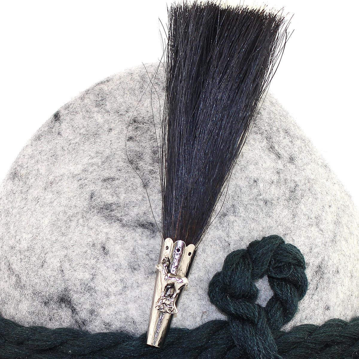 Filzhut grau mit dunklem Gamsbart, verziert durch Hirsch-Emblem und grüner Kordel.
