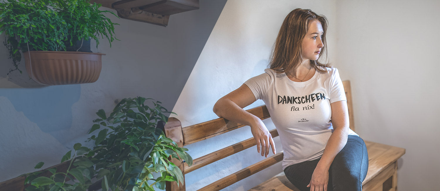 Junge Frau trägt weißes Trachten-Shirt mit bayerischem Spruch Dankscheen fia nix  auf Holzbank sitzend.