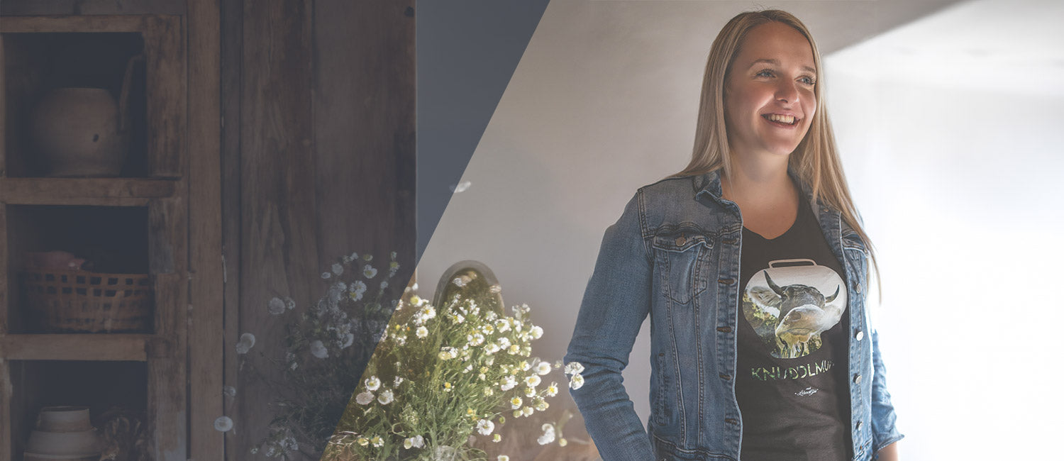Lächelnde junge Frau präsentiert ein bayerisches Damen Shirt mit Kuhglocken-Motiv in modischer Jeansjacke.