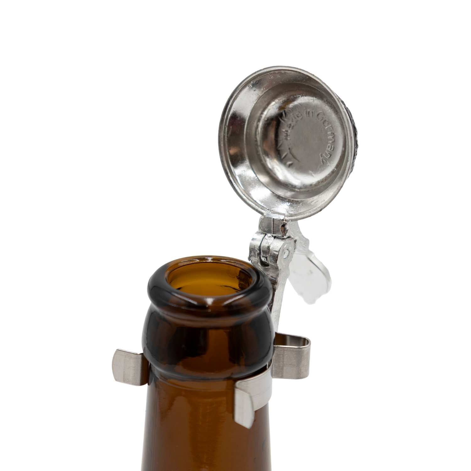 Geöffneter Bierflaschen Flachzinndeckel zum Aufstecken mit feinen Ornamenten auf einer Braunglasflasche.