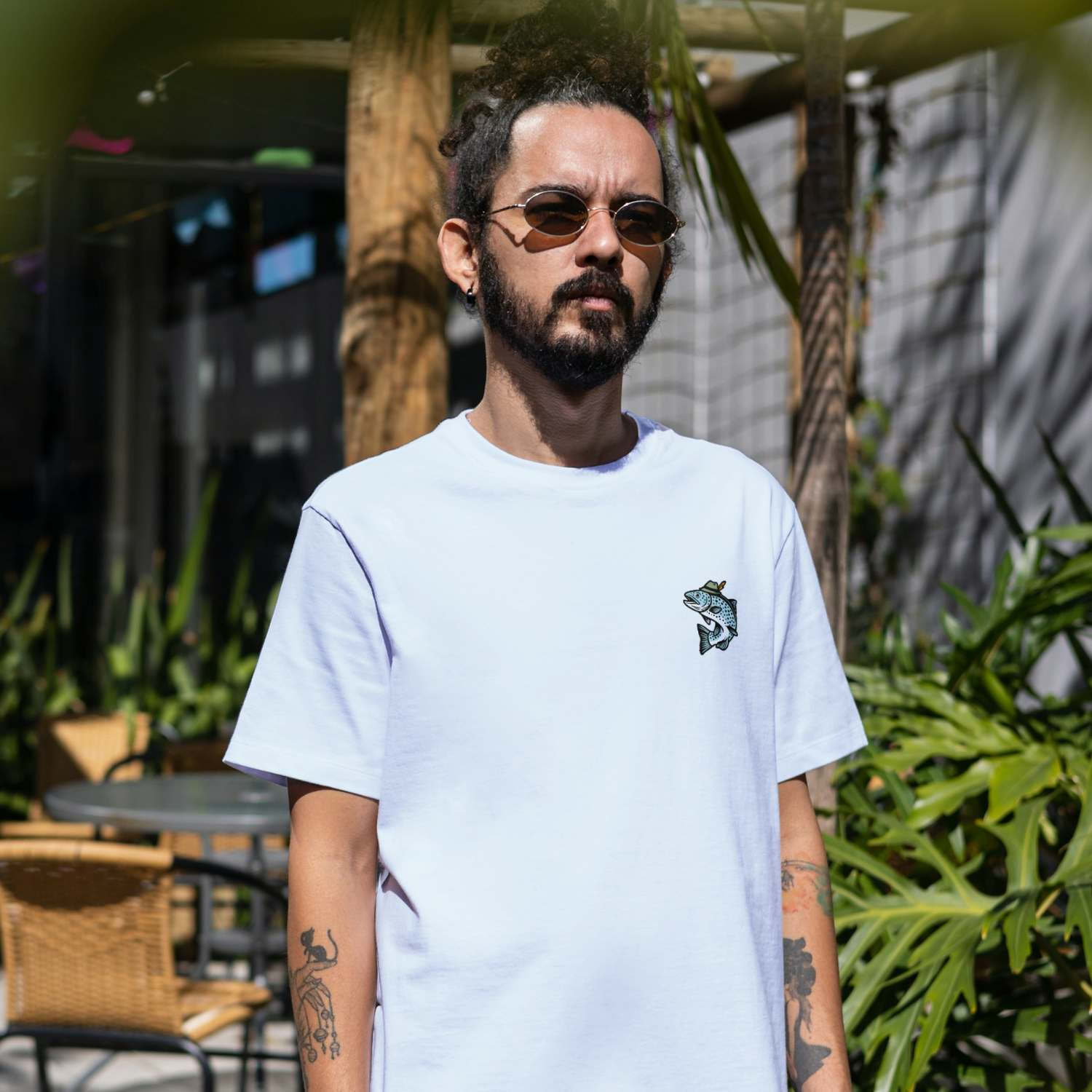 Junger Mann trägt weißes Herren T-Shirt "Boarischer Steckerlfisch" mit Fischmotiv, draußen im Sonnenlicht.