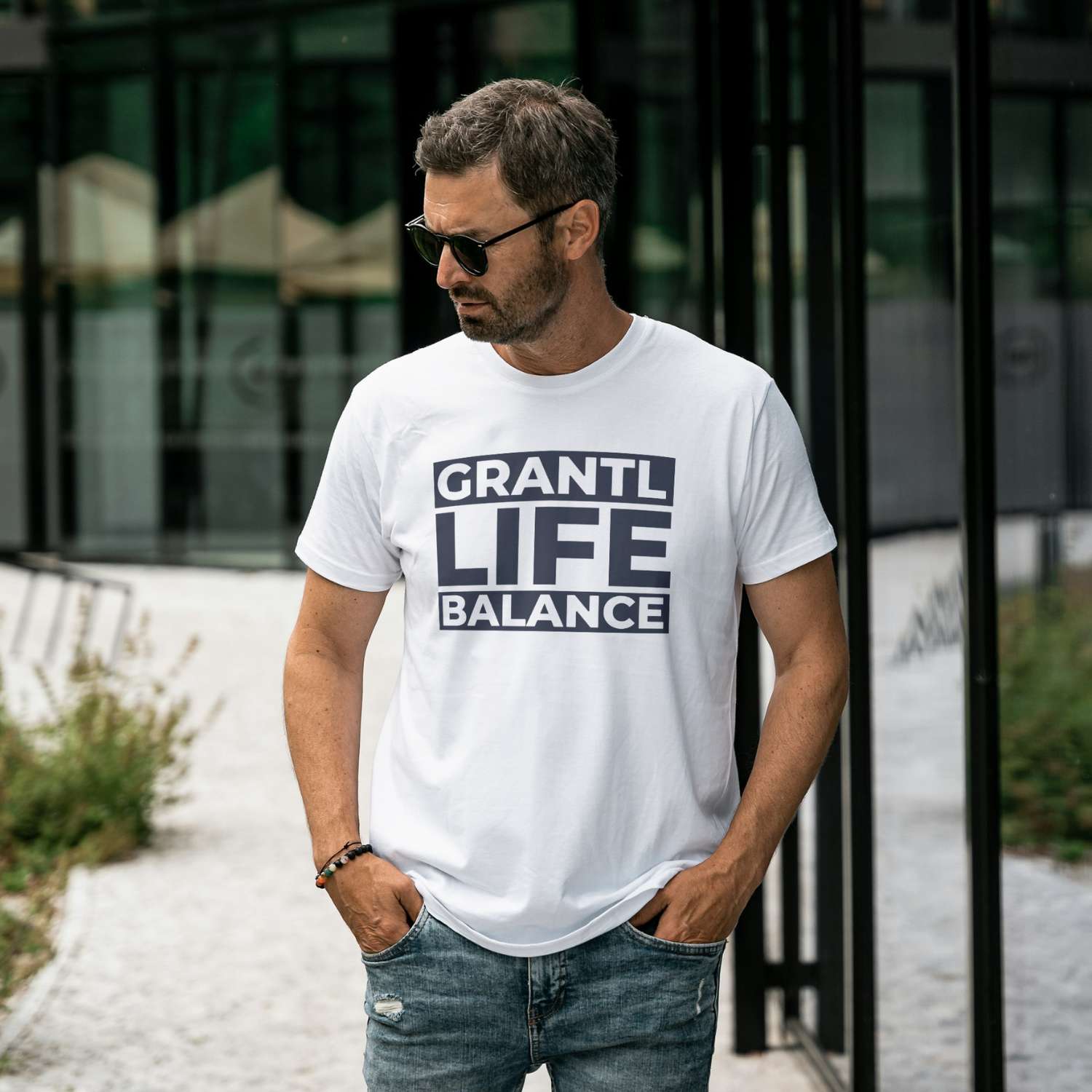Mann trägt weißes Herren T-Shirt Grantl Life Balance mit dunklem Aufdruck, Jeans und Sonnenbrille.
