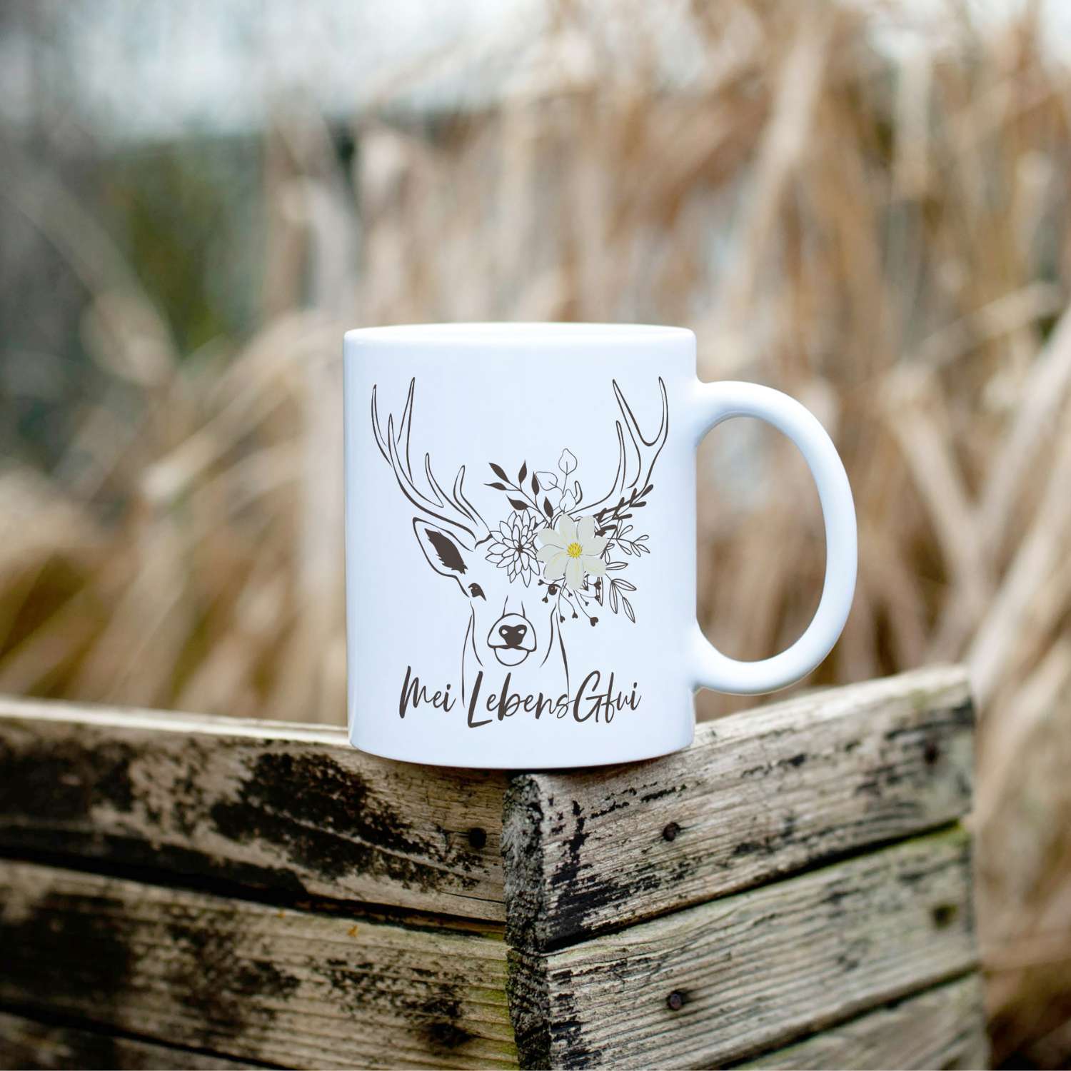 Weißer Kaffee Haferl Hirsch mit floralem Hirschkopf-Design und bayerischem Spruch auf antikem Holz.