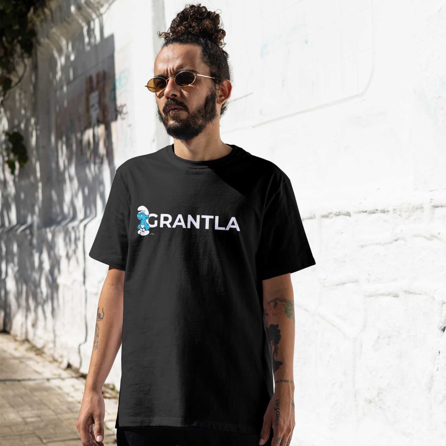 Model posiert in ®Die Schlümpfe Herren T-Shirt "Grantla" mit Schlumpf-Motiv vor weißer Wand.