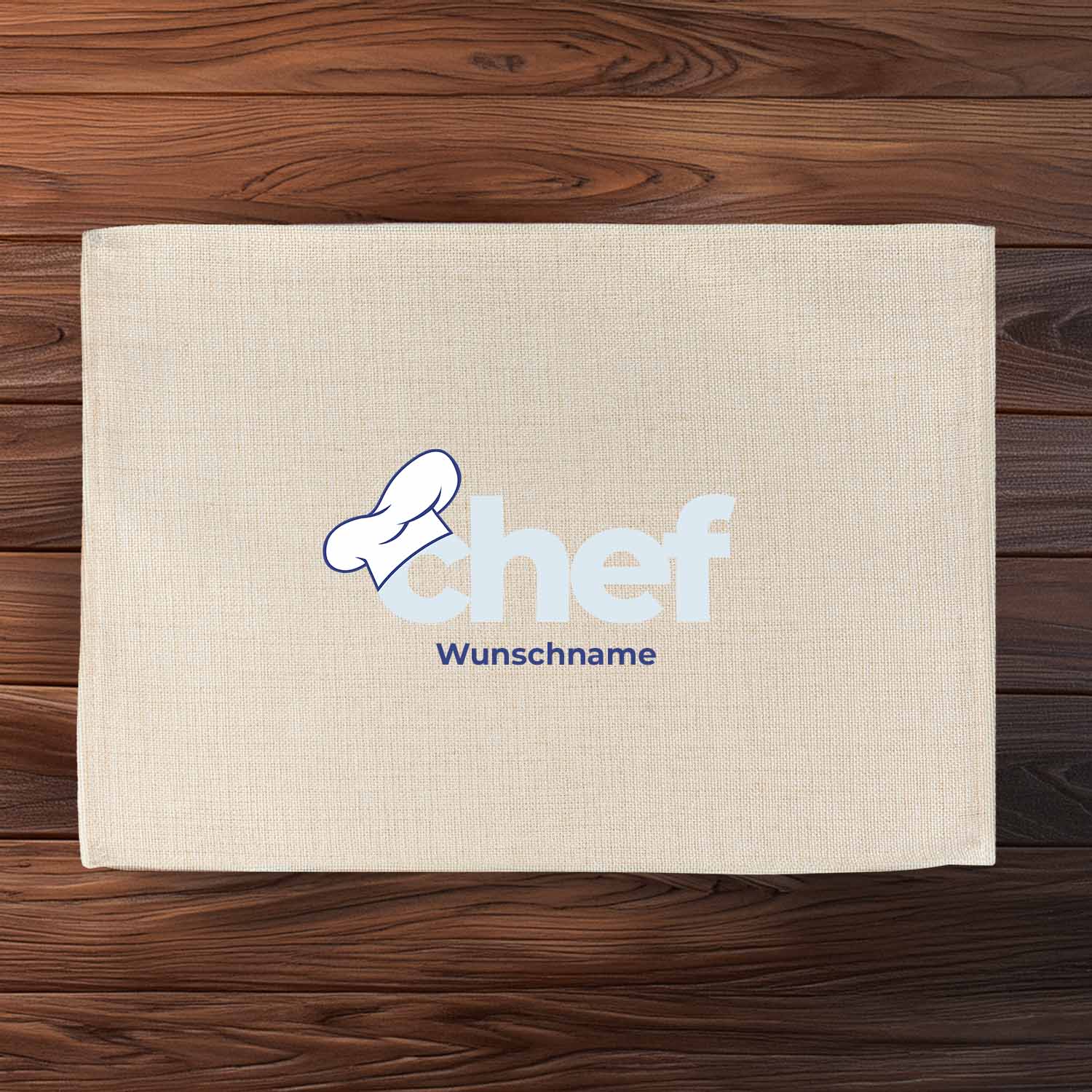 Beiges Leinen Tischset Chef mit Kochmütze und personalisierbarem Wunschname auf dunkelbraunem Holztisch.