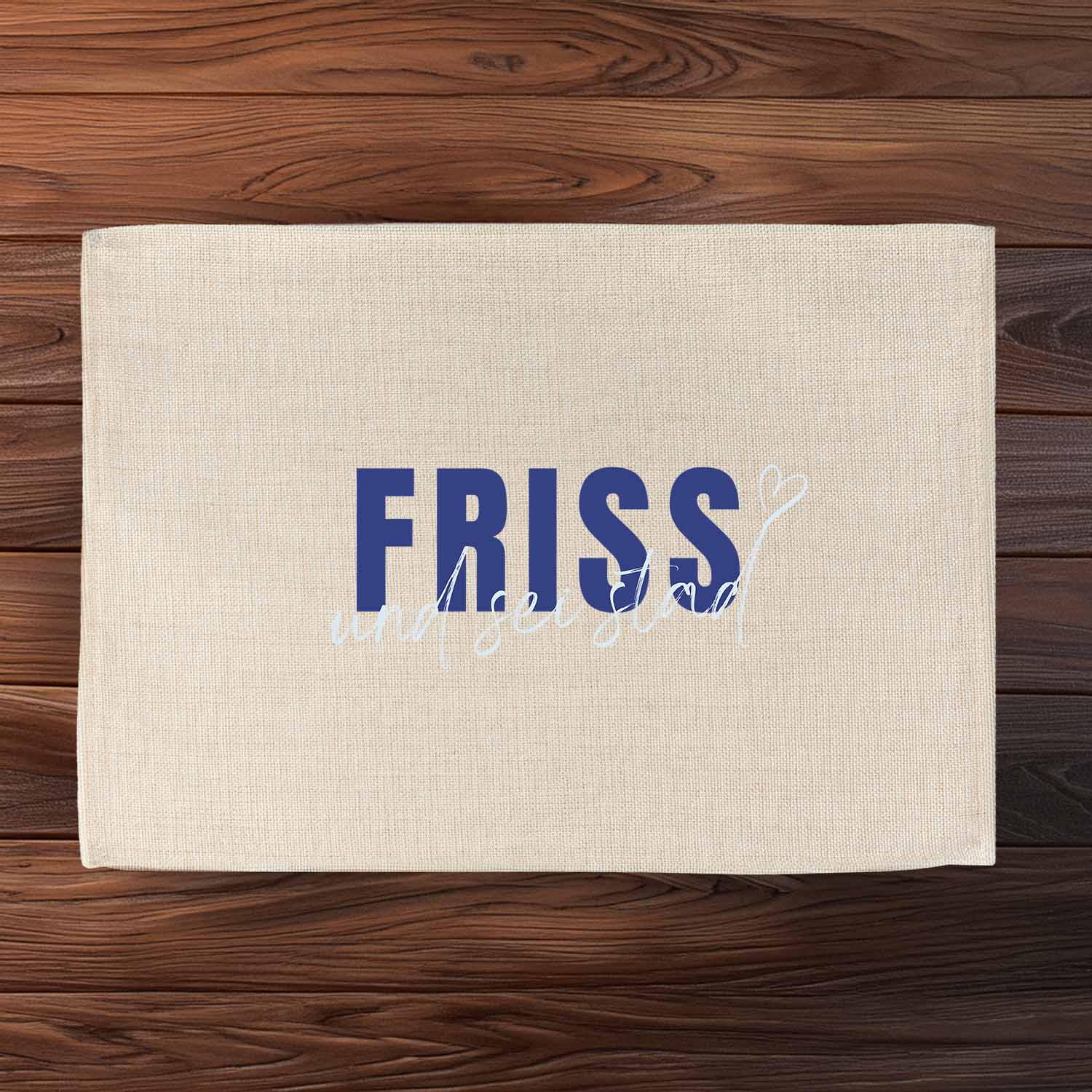 Tischset "Friss und sei stad" auf Holzuntergrund, beiges Leinen mit blauem Schriftzug, bayerischer Spruch.