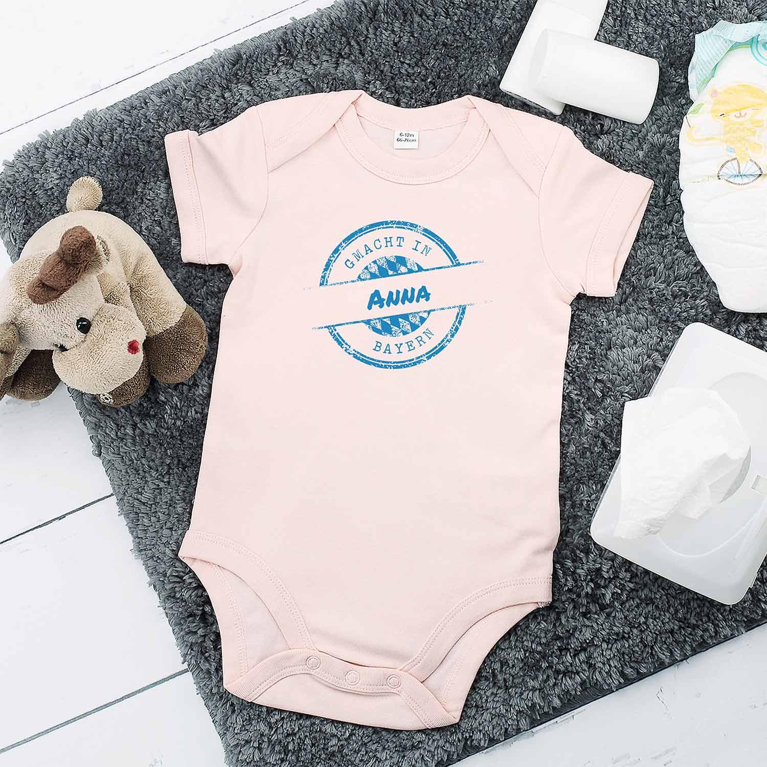 Baby Body rosa mit g'macht in Bayern und personalisiertem Wunschname Anna, auf flauschigem Teppich.