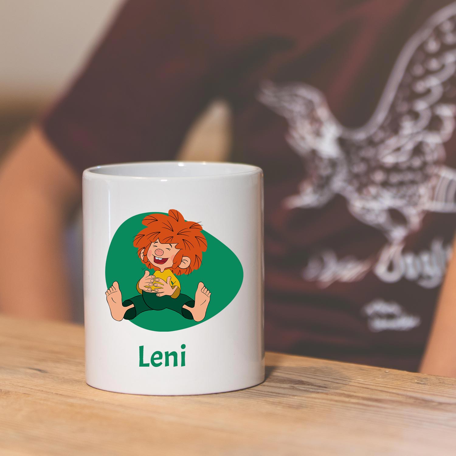 Weiße Pumuckl Tasse mit Wunschname "Leni", Kobold-Motiv und lachendem Pumuckl auf Holztisch