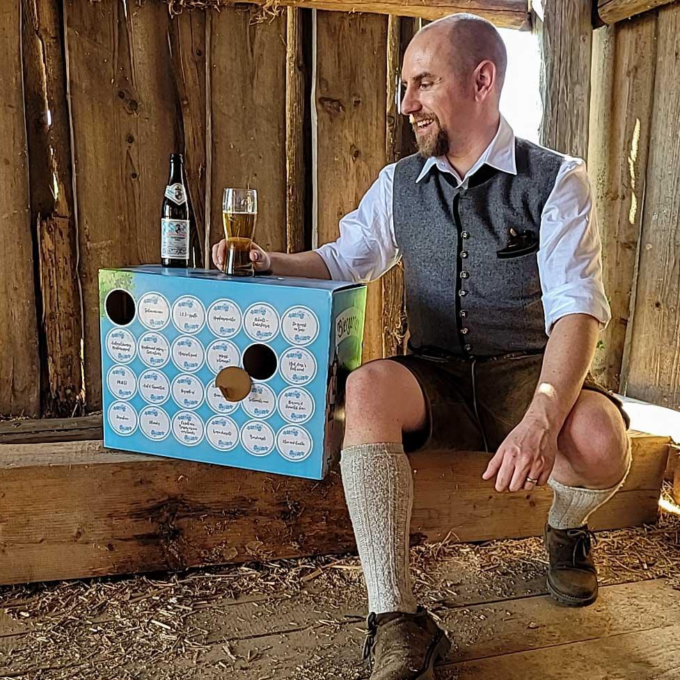Mann in Tracht genießt Bier aus Glas neben der blauen Bier-Box Bayerischer Biergarten auf Holzbalken.