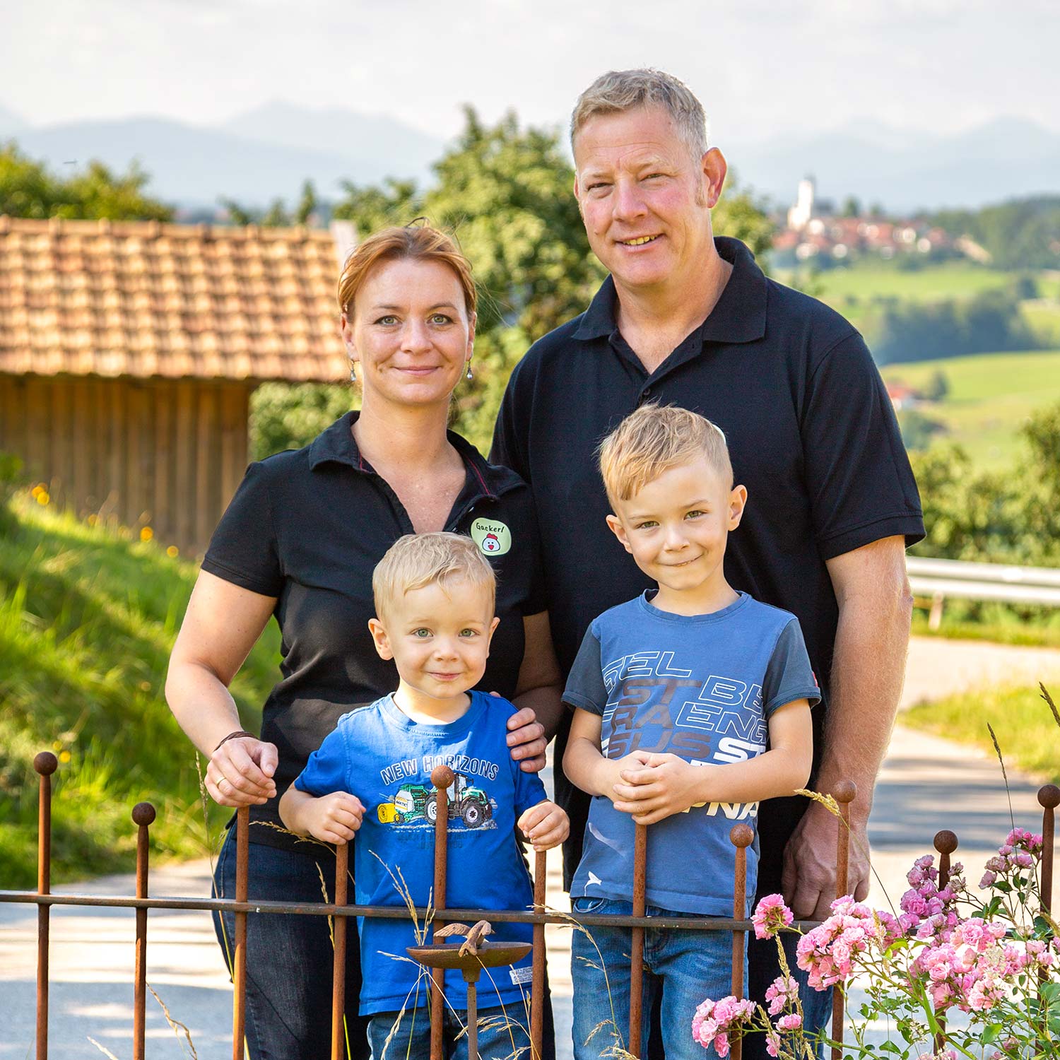 Glückliche Familie mit zwei kleinen Jungen vor malerischer Alpenlandschaft und Dorfkirche im Hintergrund stehend