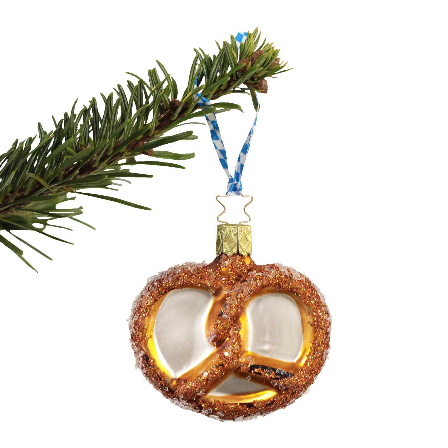 Glänzender Brezel-Weihnachtsanhänger, goldbraun, mit glitzerndem Salz und blau-weißem Band am Tannenzweig.