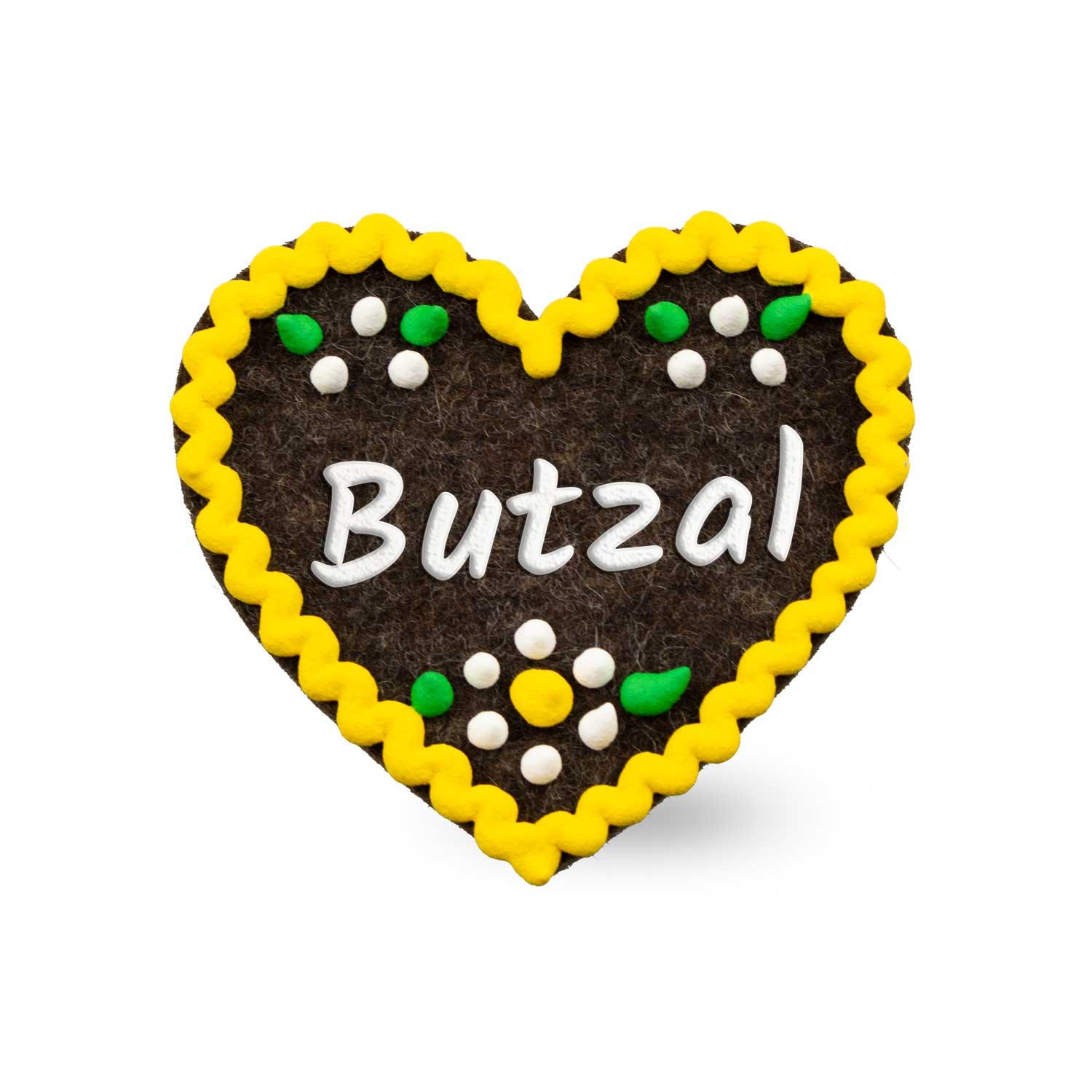 Brauner Filzherz-Anstecker Butzal mit gelbem Rand, weißer Schrift und bunten Filzblumen-Details.