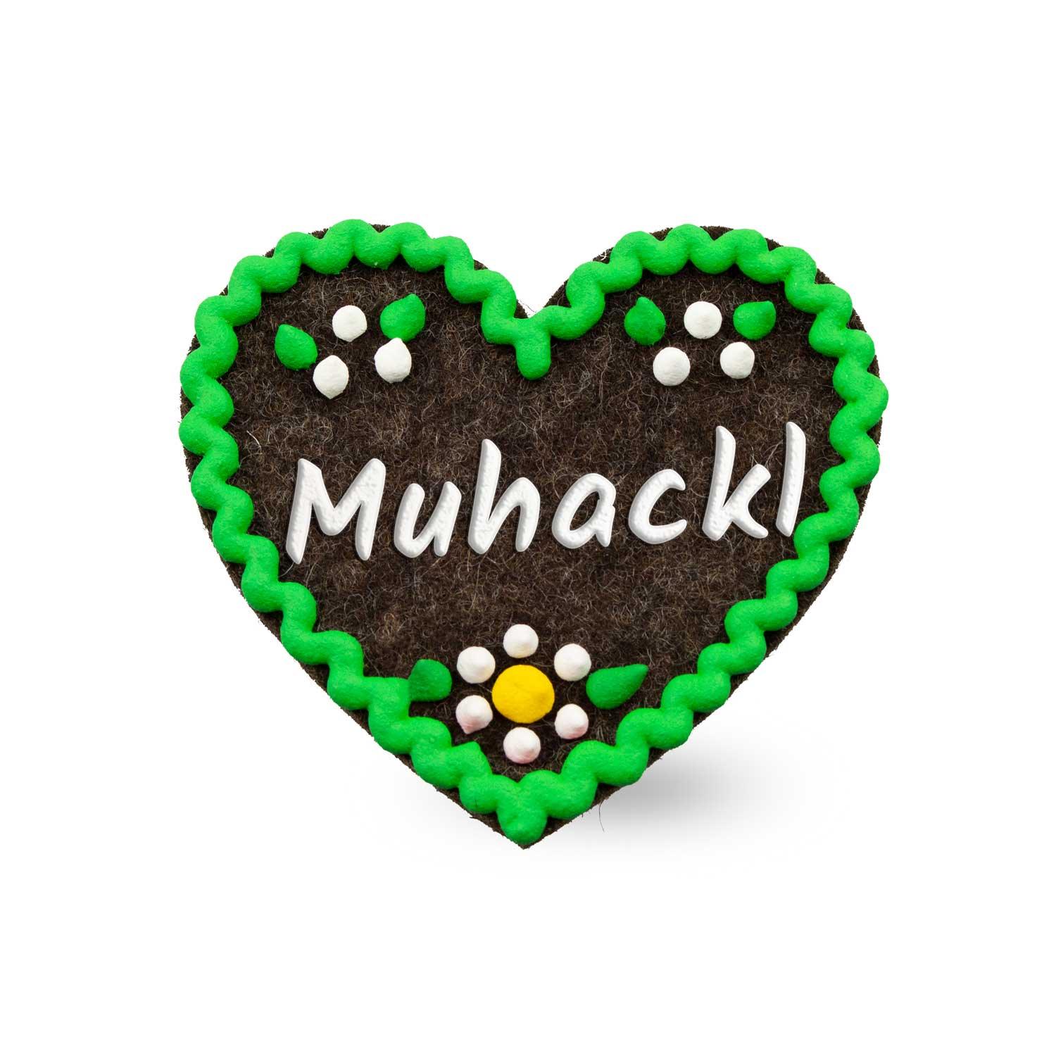 Liebevoller Filzherz-Anstecker "Muhackl" in Braun und Grün, verziert mit weißen Blumen und Schriftzug.