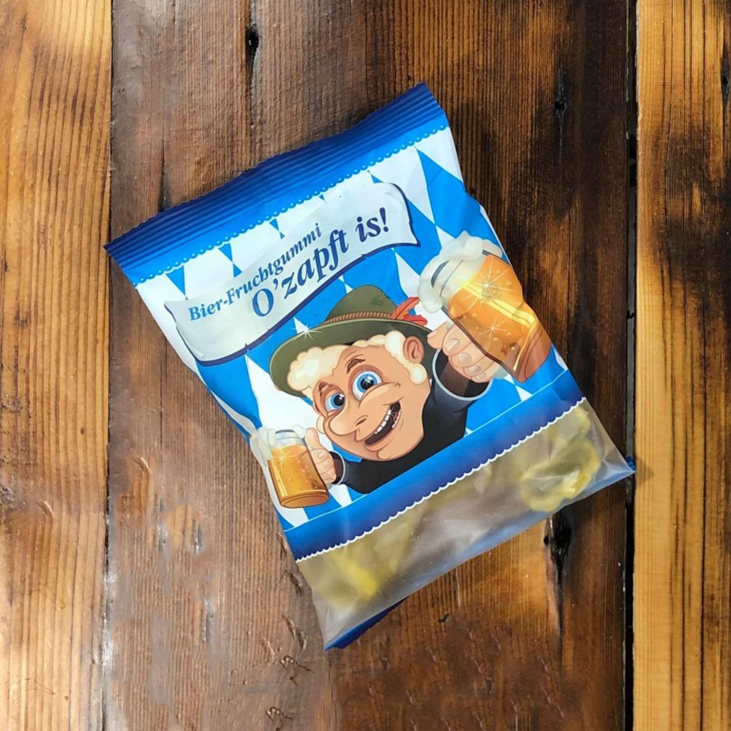 Verpackung von Bier-Fruchtgummi O'zapft is mit bayerischem Rautenmuster und Cartoon-Figur auf Holztisch.