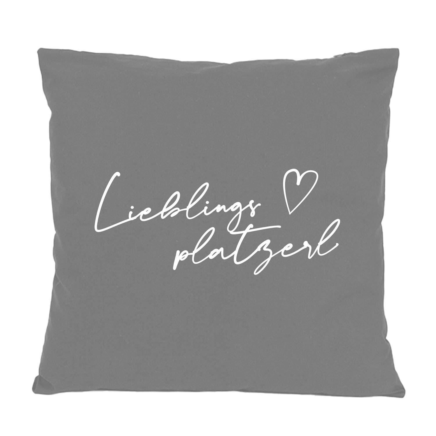 Graues Kissen mit der weißen Aufschrift Lieblingsplatzerl und Herzsymbol. Dekokissen für Wohnzimmer.
