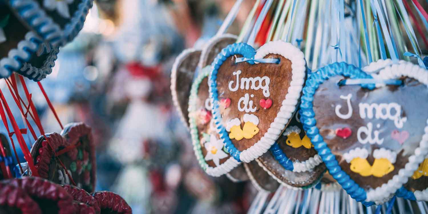Reihe von traditionellen Lebkuchenherzen mit bayerischem Spruch "I mog di", weißem Zuckerguss und blauen/roten Bändern.