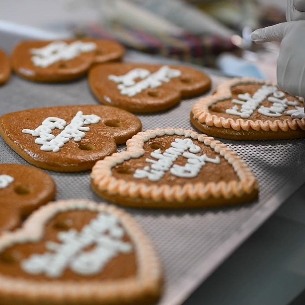 Herzförmige Lebkuchen, frisch gebacken und mit weißem Zuckerguss verziert, auf einem Backblech.